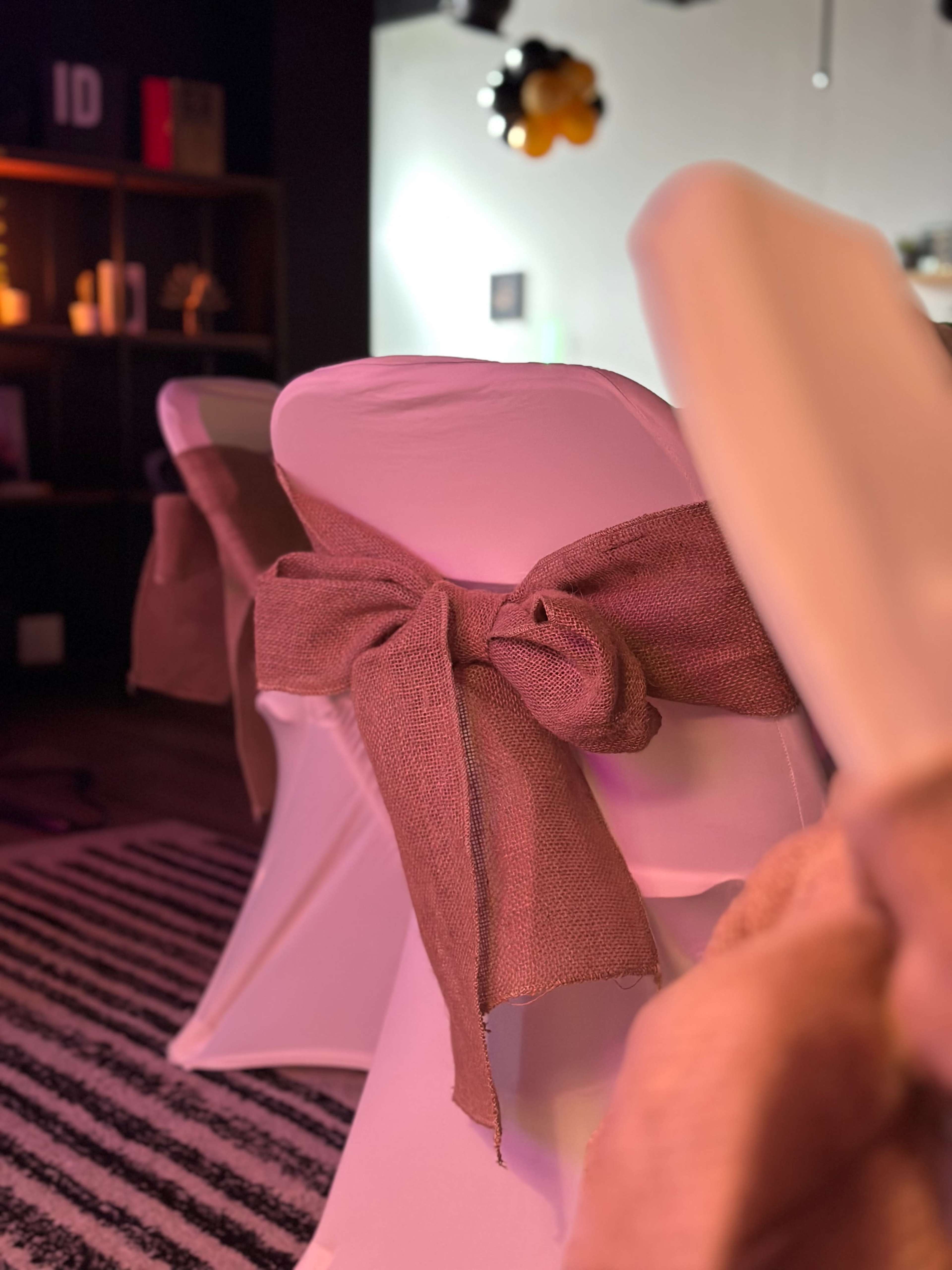 The image shows a close-up of a chair draped in a white cover secured with a brown burlap bow.