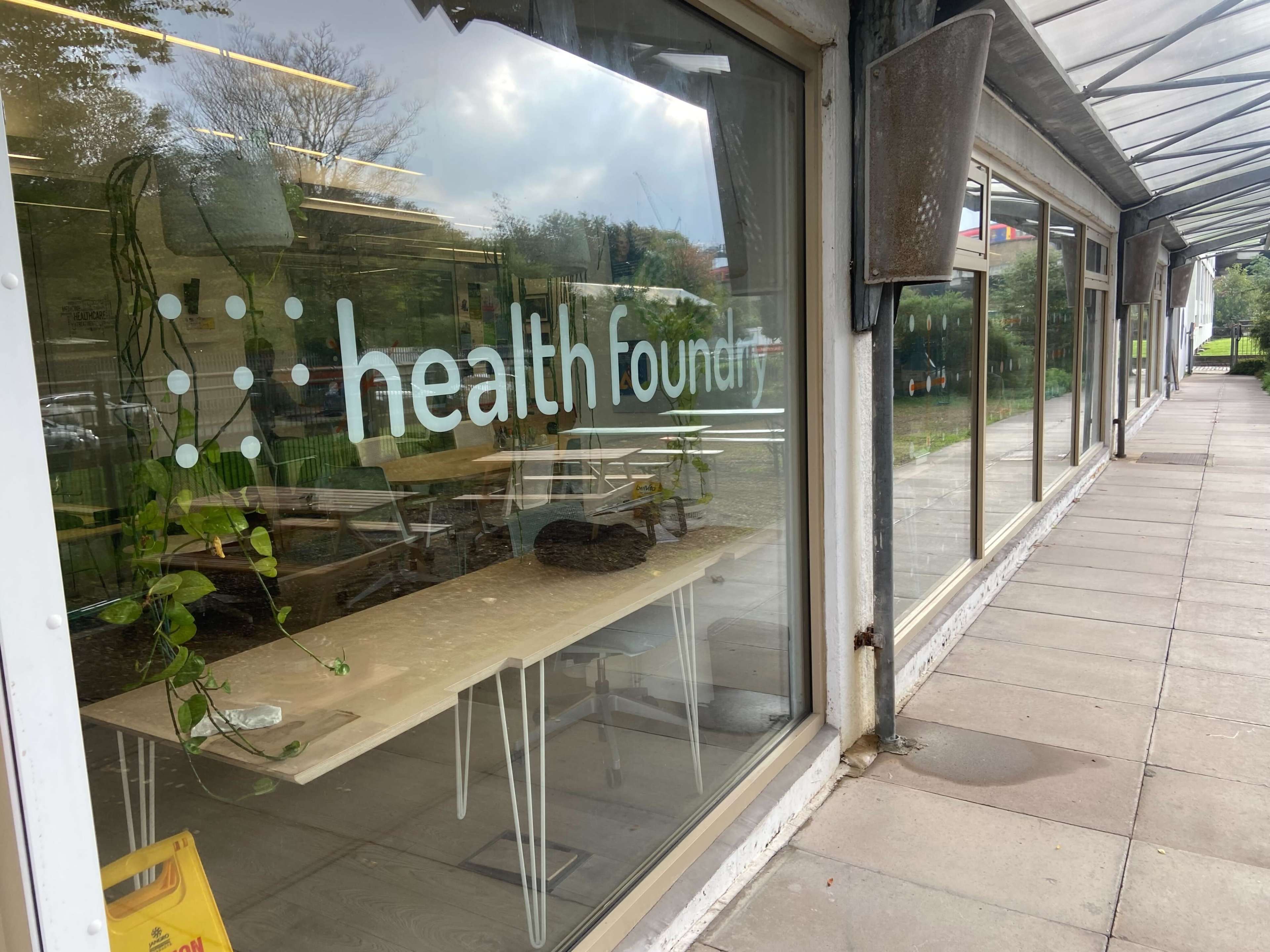 A glass storefront with the sign "health founder" and visible indoor seating area, surrounded by planters and a covered walkway.