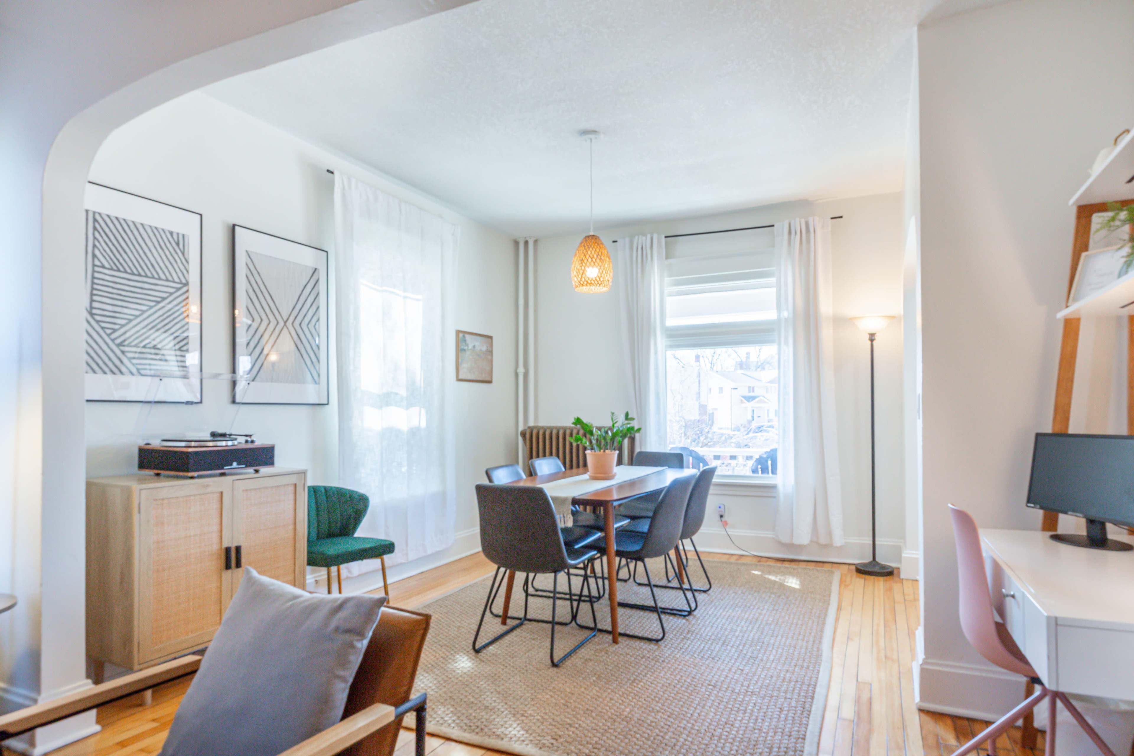 A well-lit dining area features a table surrounded by chairs, with a mix of modern decor and natural light flowing through large windows.