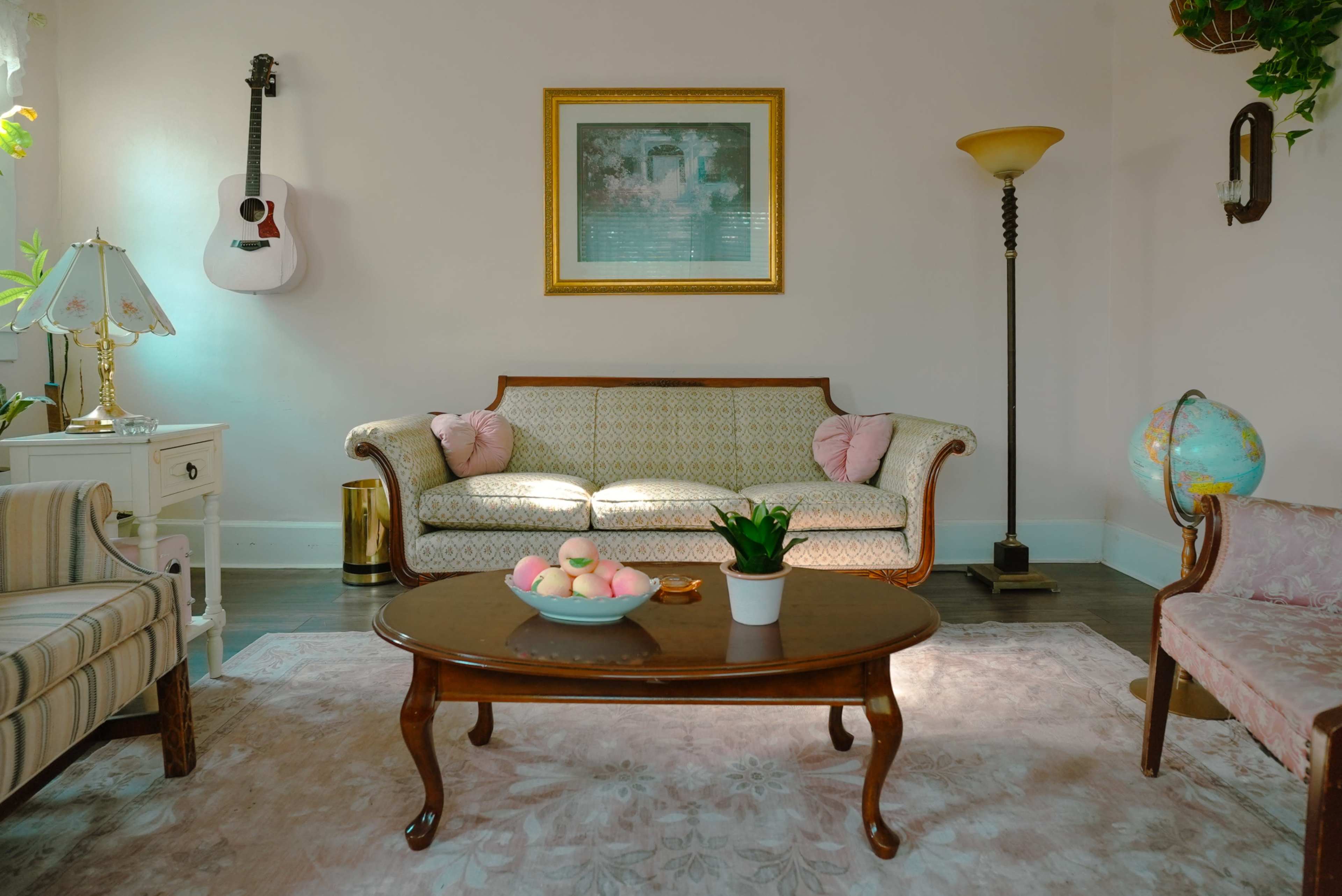 The living room features a vintage sofa and armchair, a round wooden coffee table, and a globe in a corner, with a guitar hanging on the wall and a framed picture above the couch.