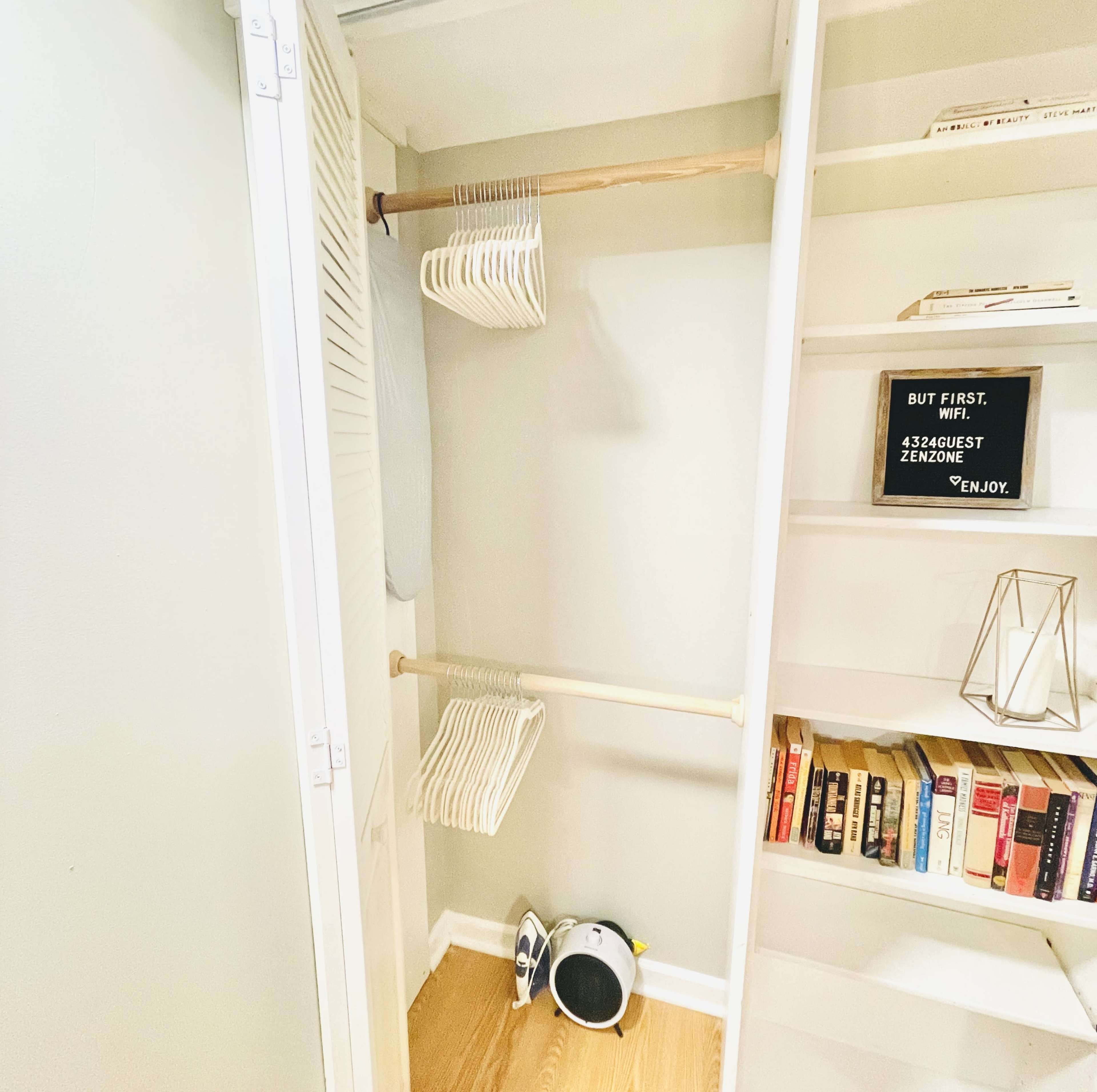 The image shows a small closet with two wooden rods holding empty hangers, a shelf with books, and a decorative sign on a nearby wall.