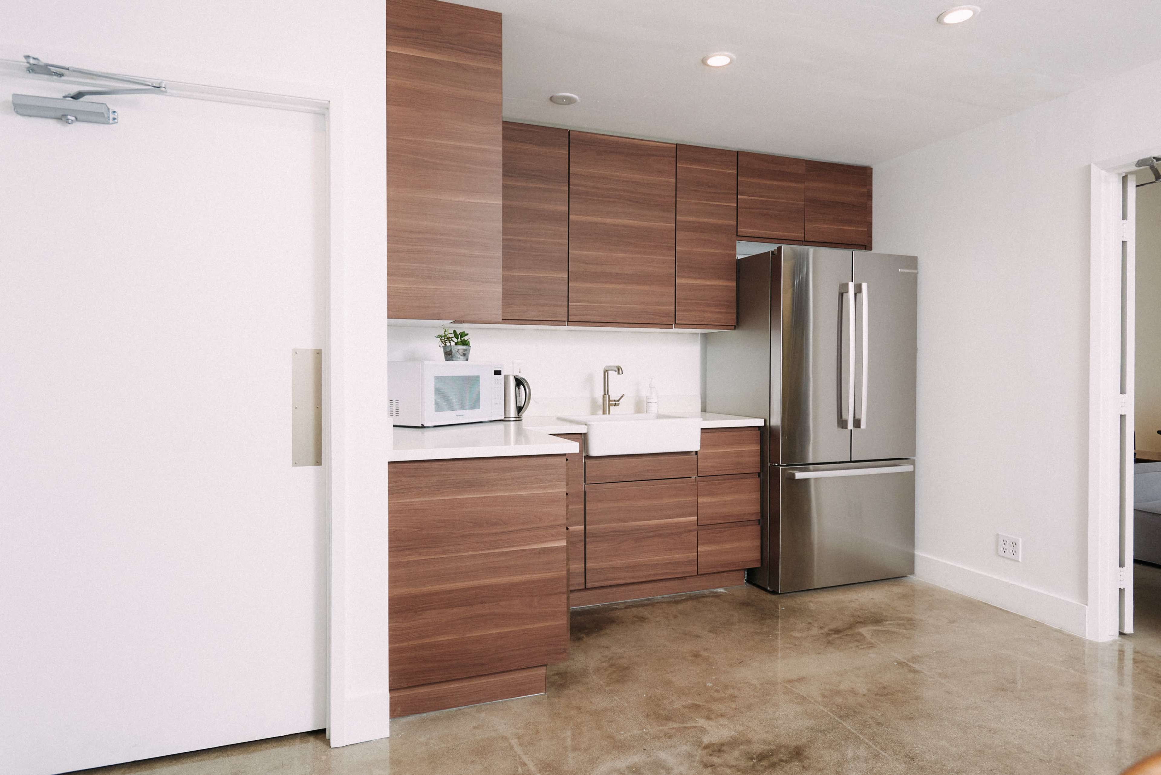 A modern kitchen featuring wooden cabinets, a stainless steel refrigerator, a white sink, and a microwave on the countertop.