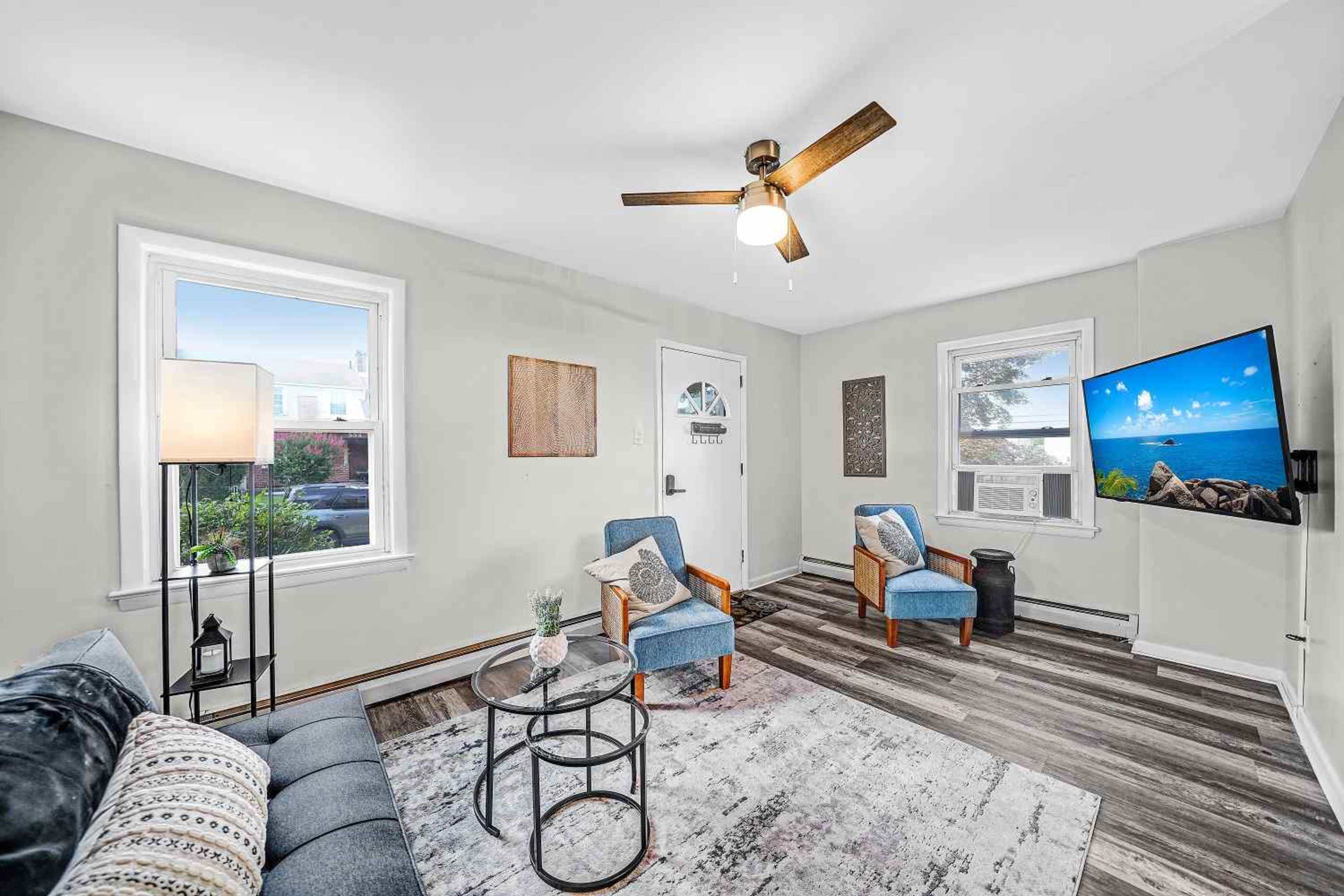 A living room with a light green wall, two blue chairs, a gray sofa, a coffee table, and a wall-mounted television.
