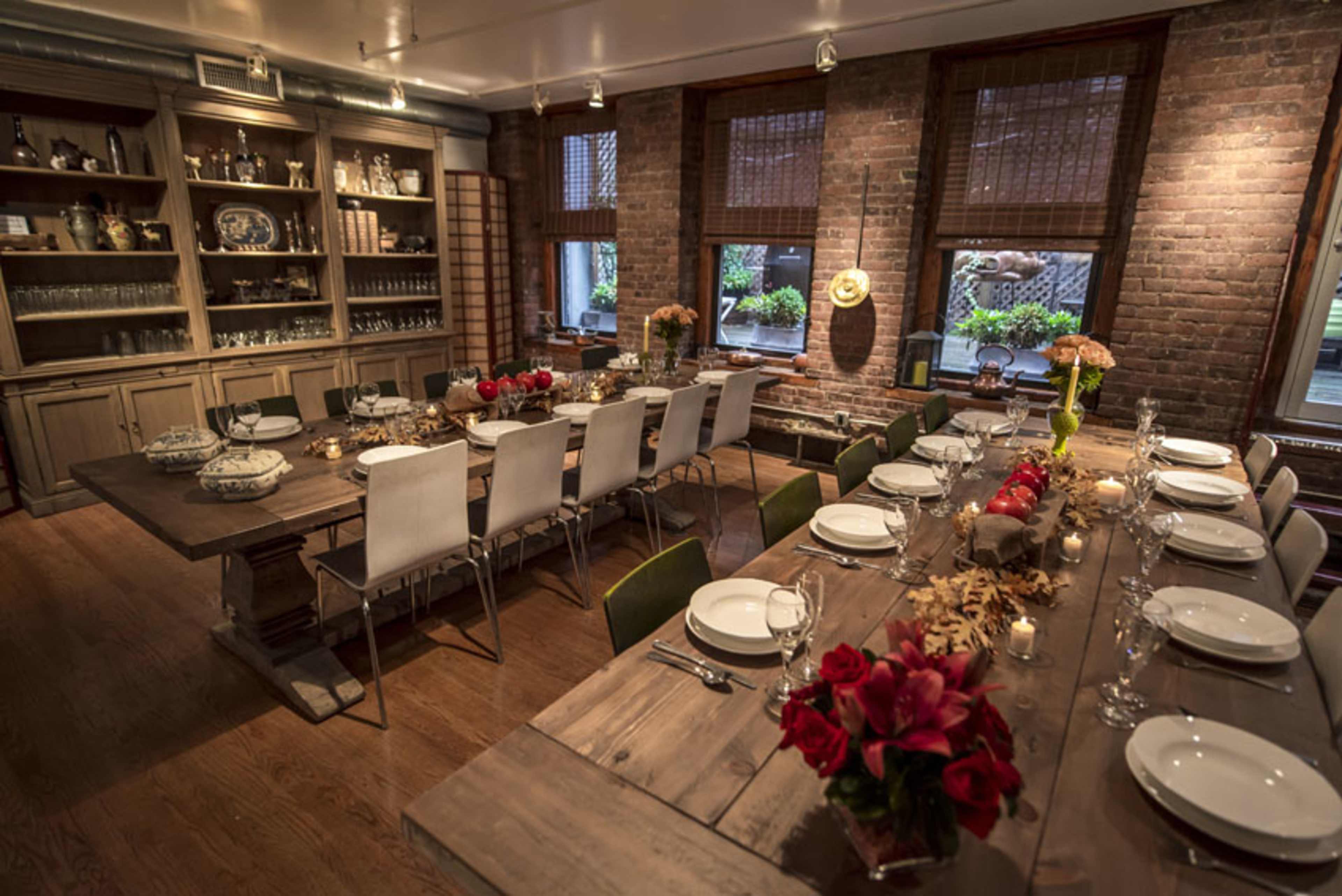 A dining room with a long wooden table set for a meal, surrounded by chairs and decorated with flowers and candles.