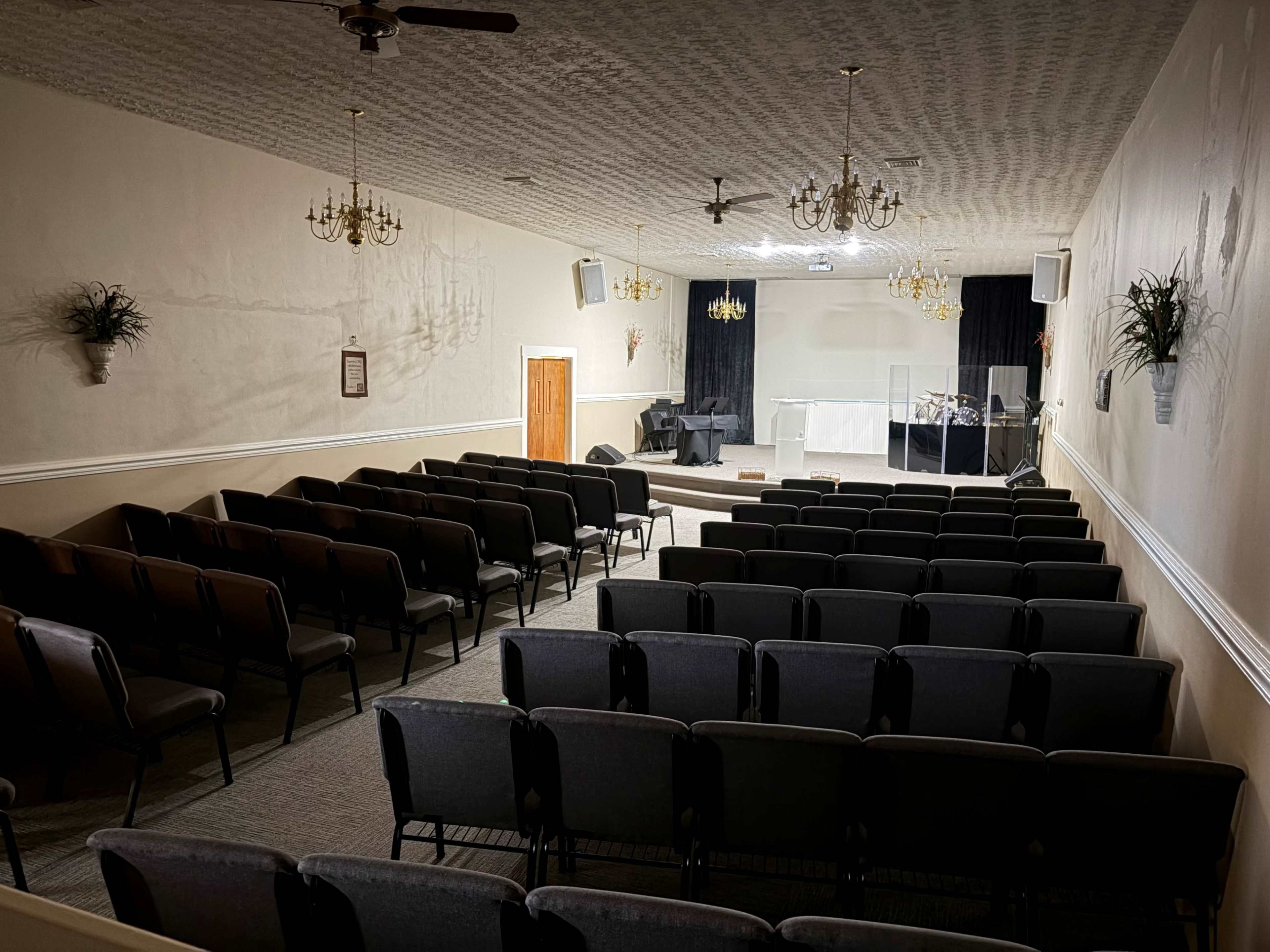 The image shows an empty church interior with rows of chairs facing a stage area, featuring a microphone stand and musical instruments.