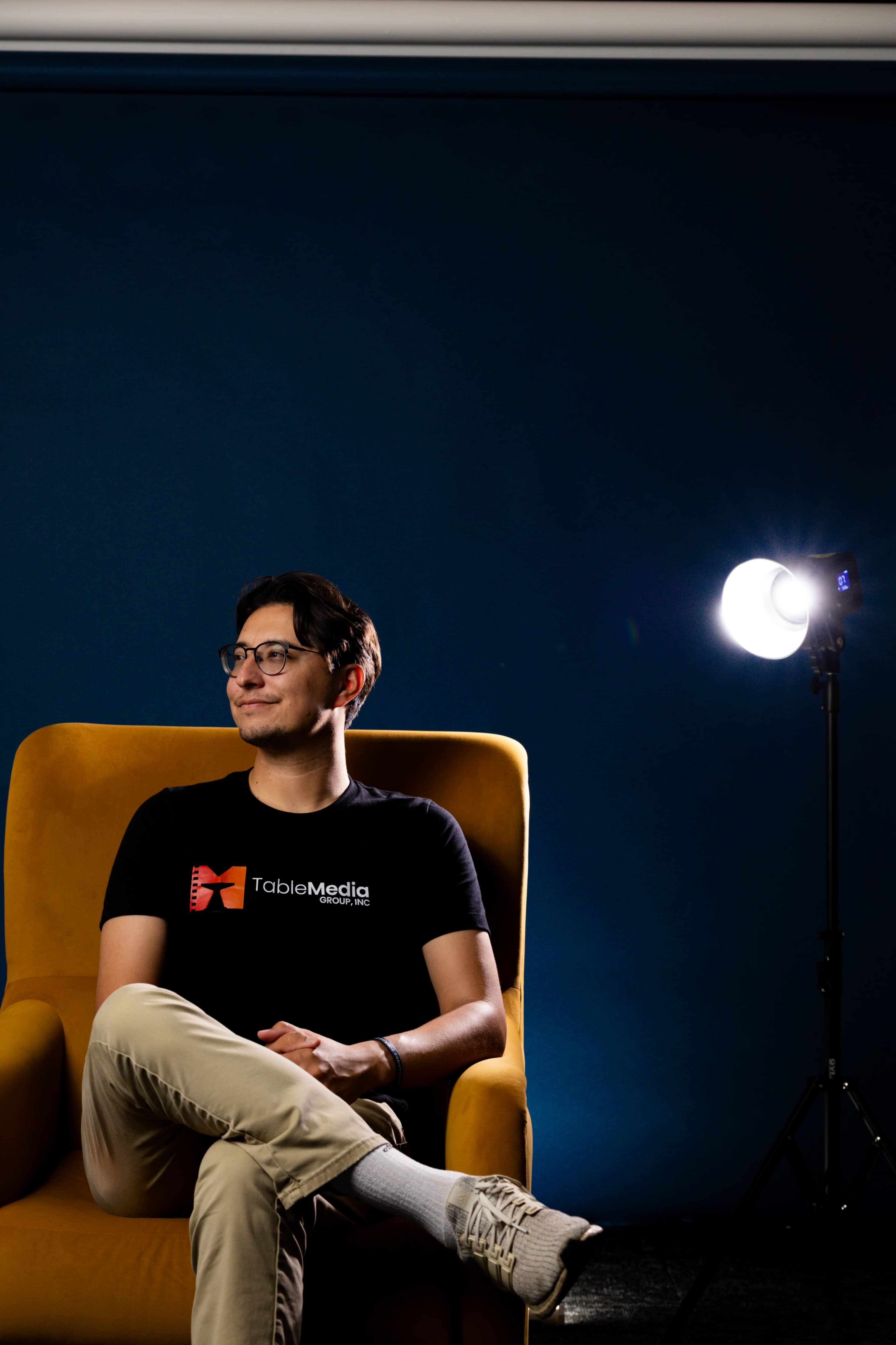 A person sits in a yellow armchair against a blue wall, with a spotlight illuminating the scene.