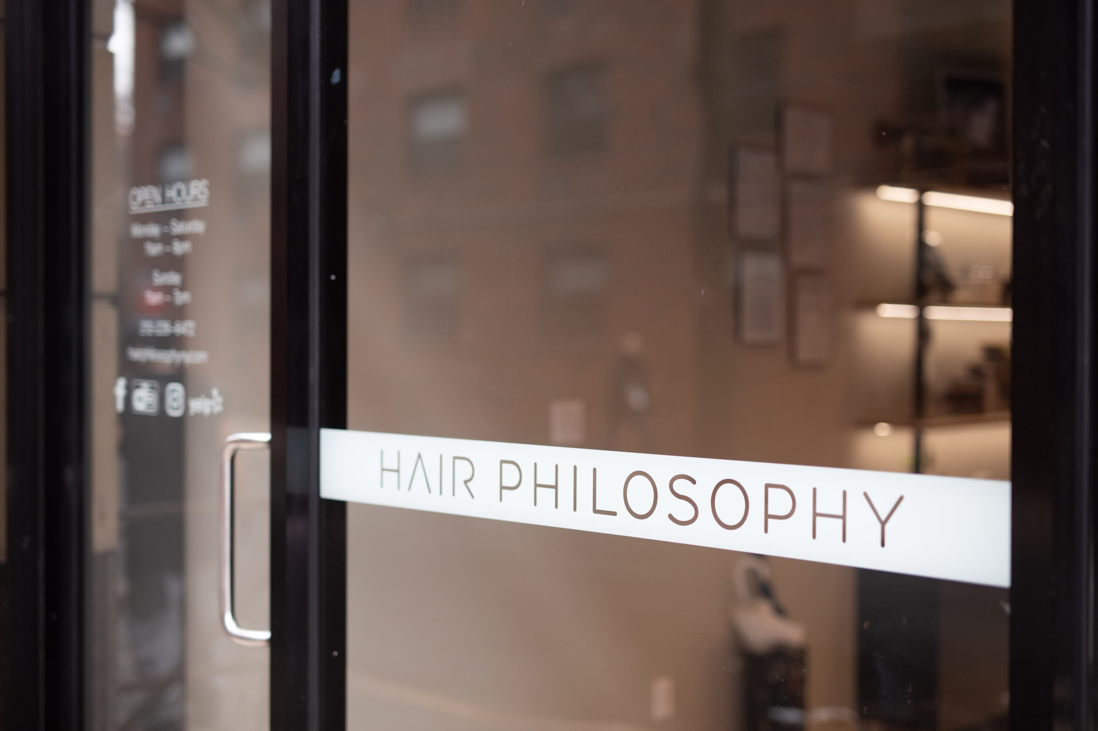 The entrance of a salon named "Hair Philosophy," featuring glass doors with clear branding and operating hours.