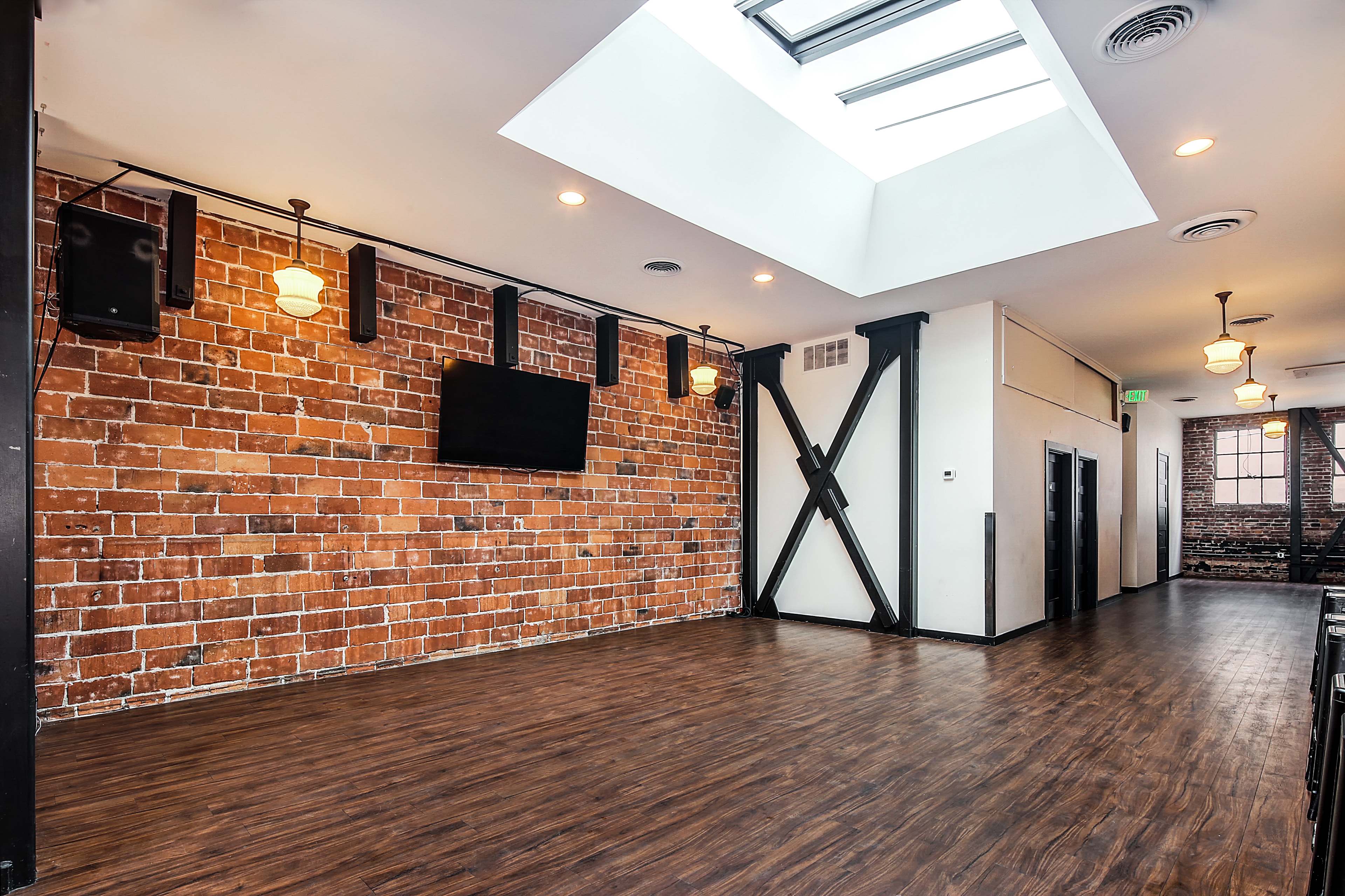 The interior features a sunlit room with a brick wall, hardwood flooring, and modern lighting fixtures.