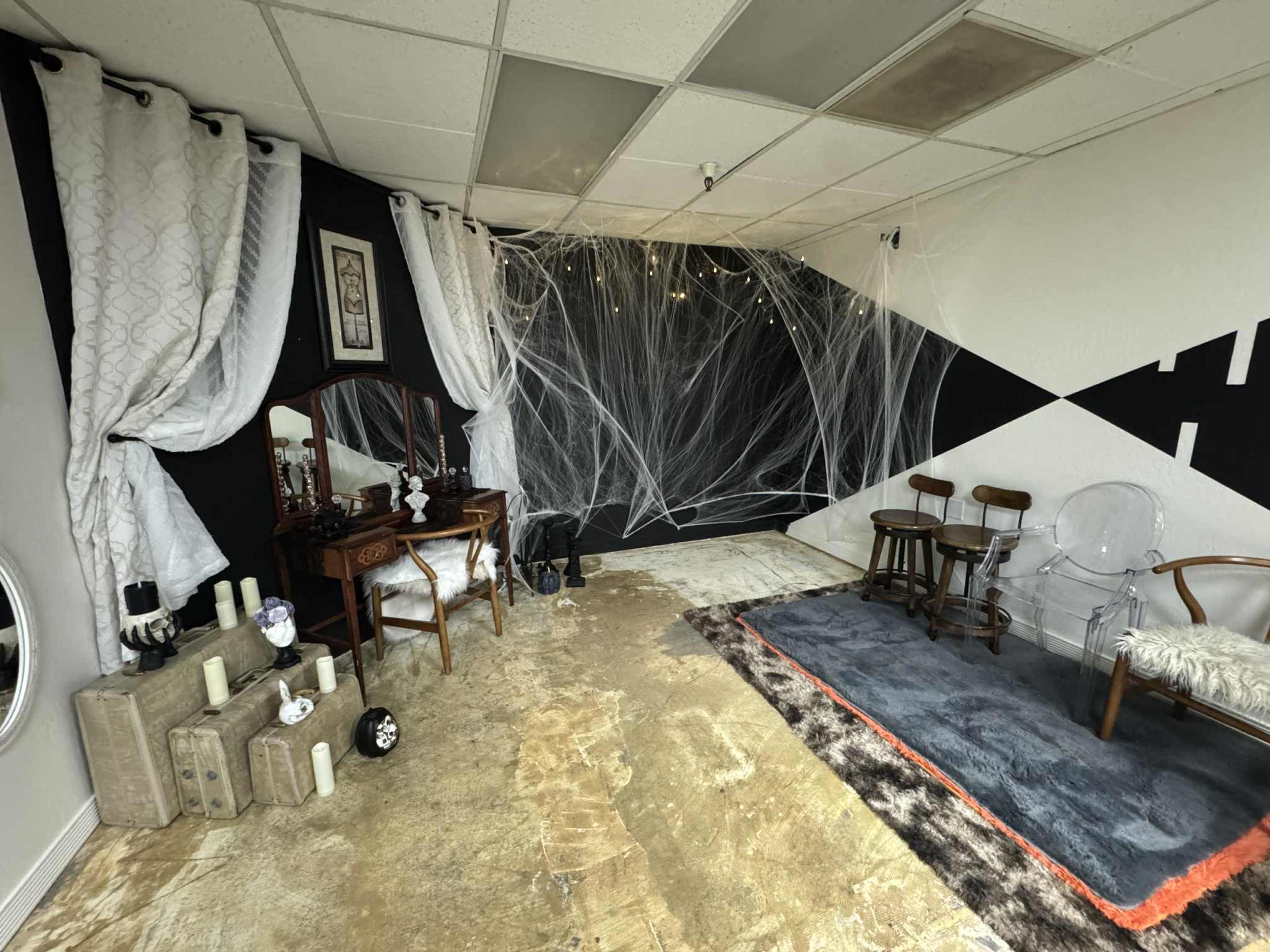 The image shows a room with a combination of a vintage-style vanity, chairs, and draped fabric, alongside a wall featuring a geometric black and white design.
