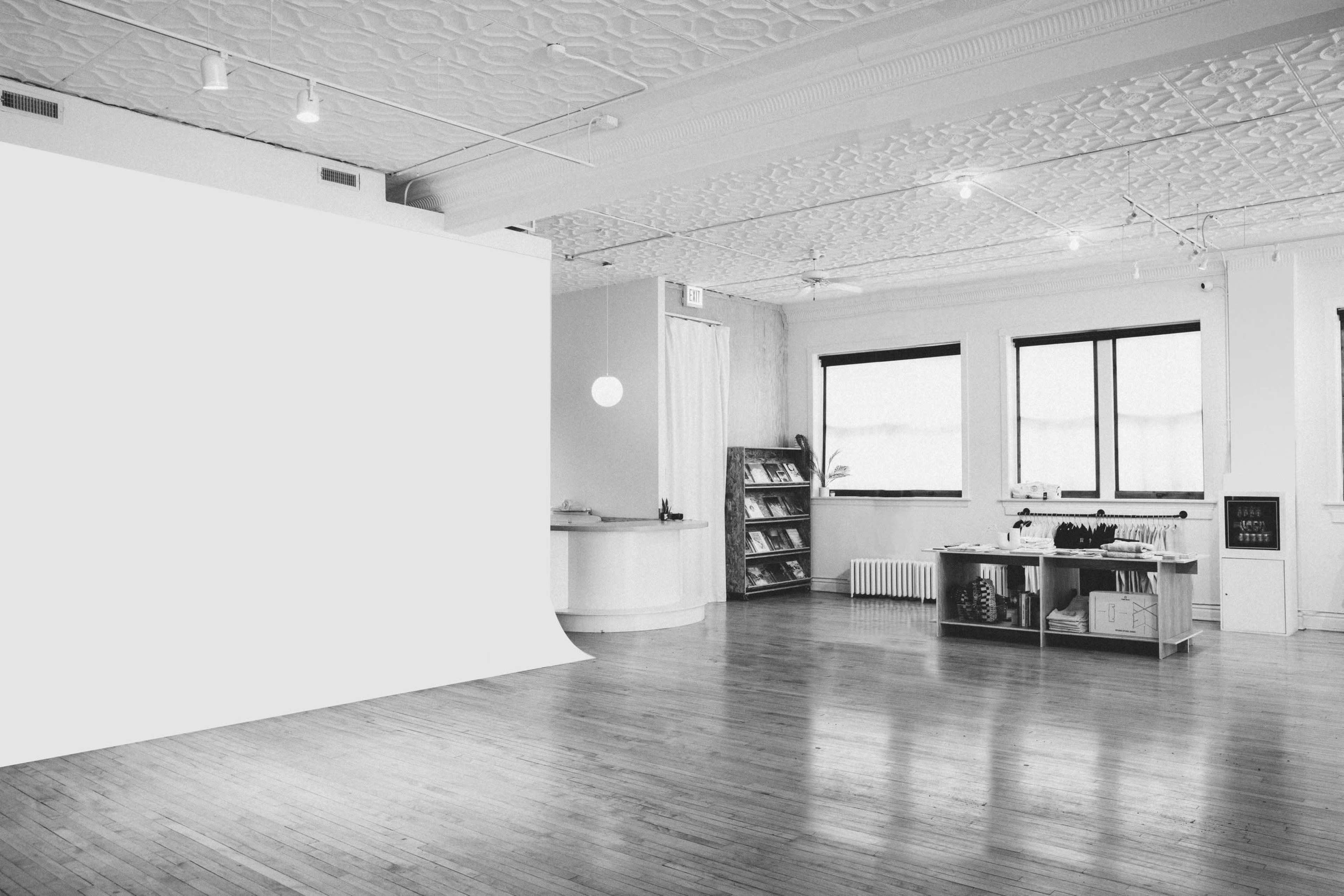 The image shows a spacious, well-lit studio with a white backdrop, large windows, and a shelving unit filled with various items.