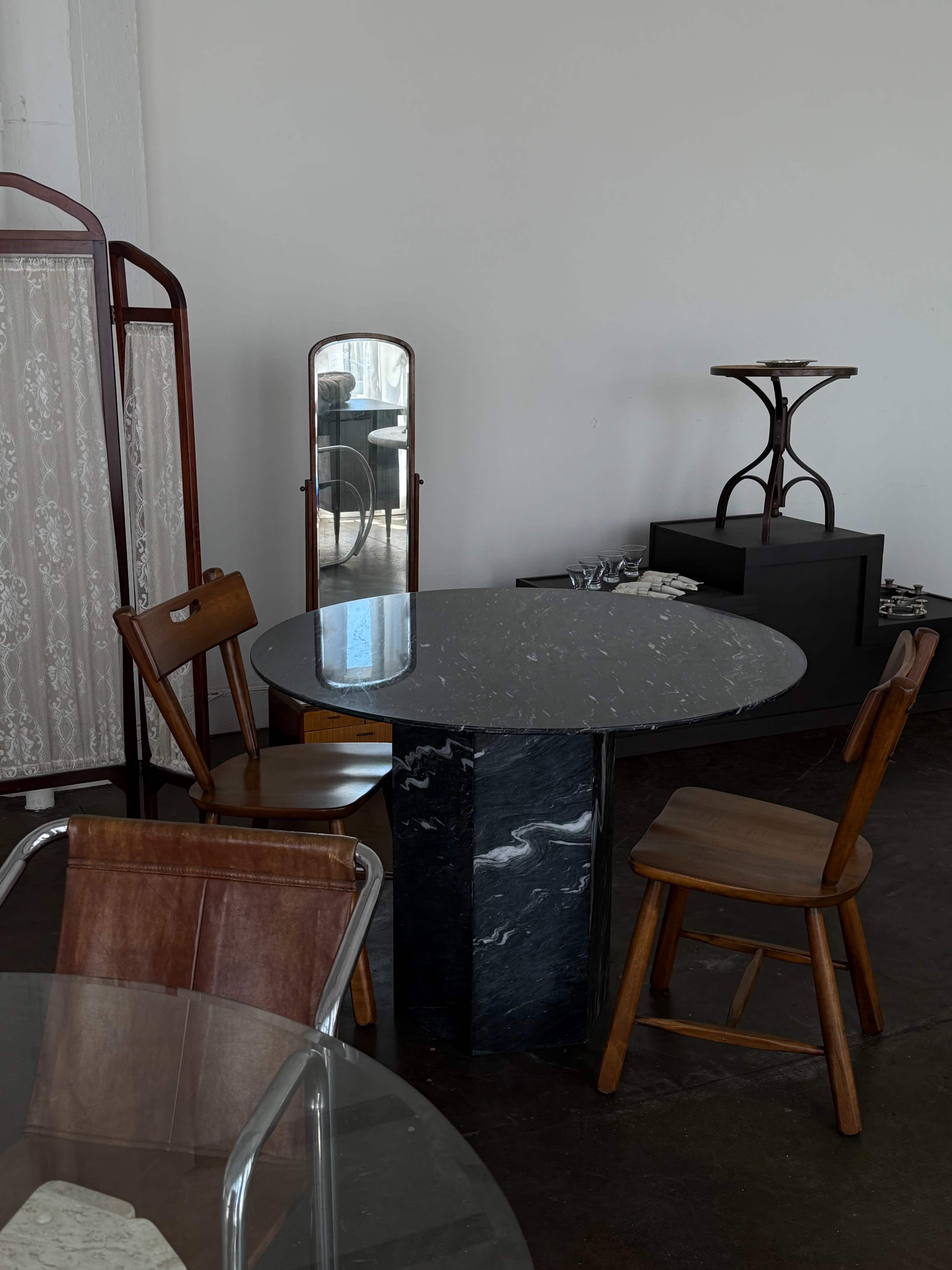 A round marble table is positioned in a room with various chairs and a mirror in the background.