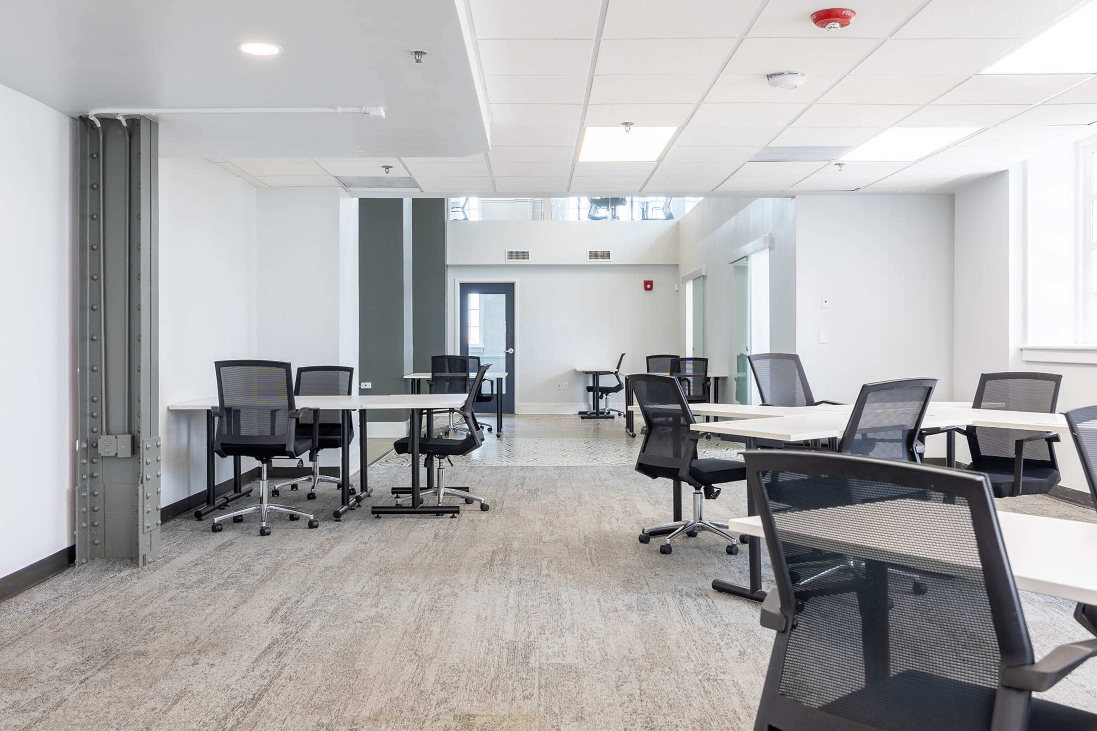 The image shows a modern, open office space with several empty desks and ergonomic chairs arranged throughout.