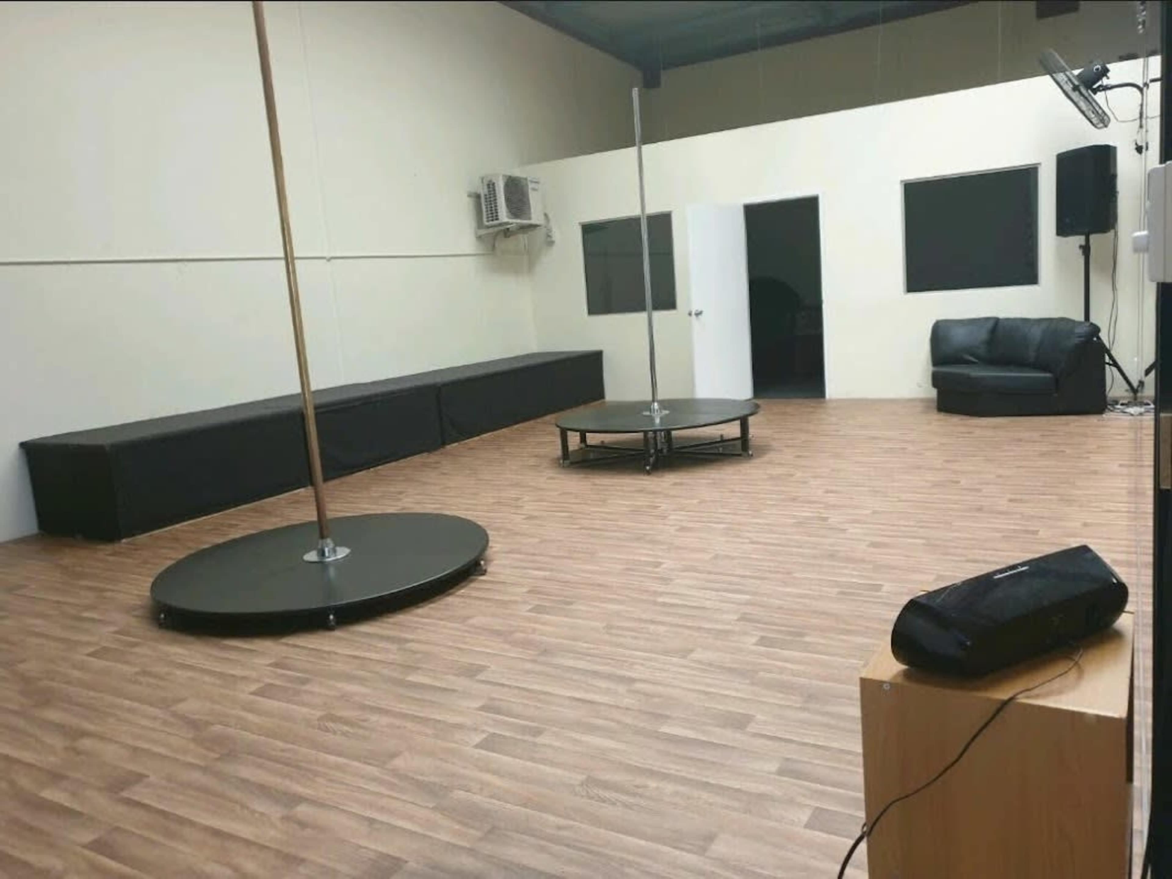 A spacious room featuring two freestanding poles, a circular table in the center, a black sofa against one wall, and a wooden floor.