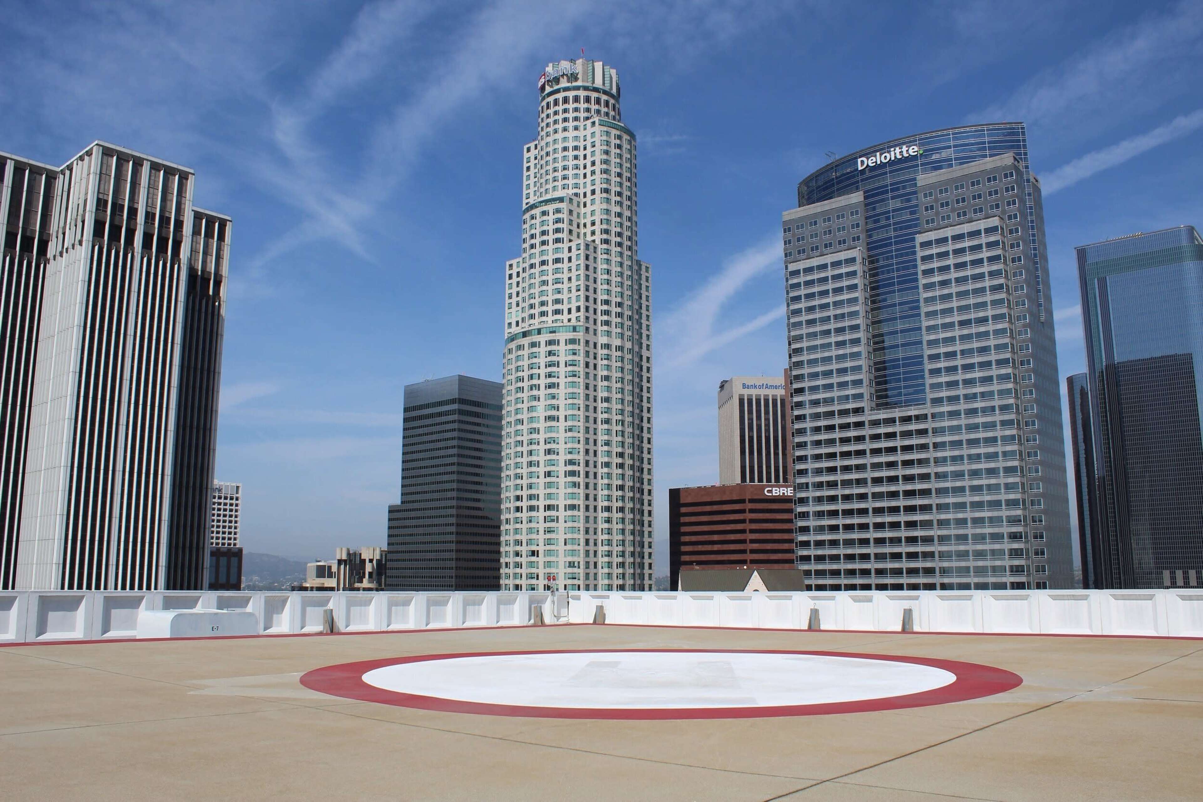 A rooftop helipad surrounded by several high-rise buildings in an urban skyline against a blue sky.