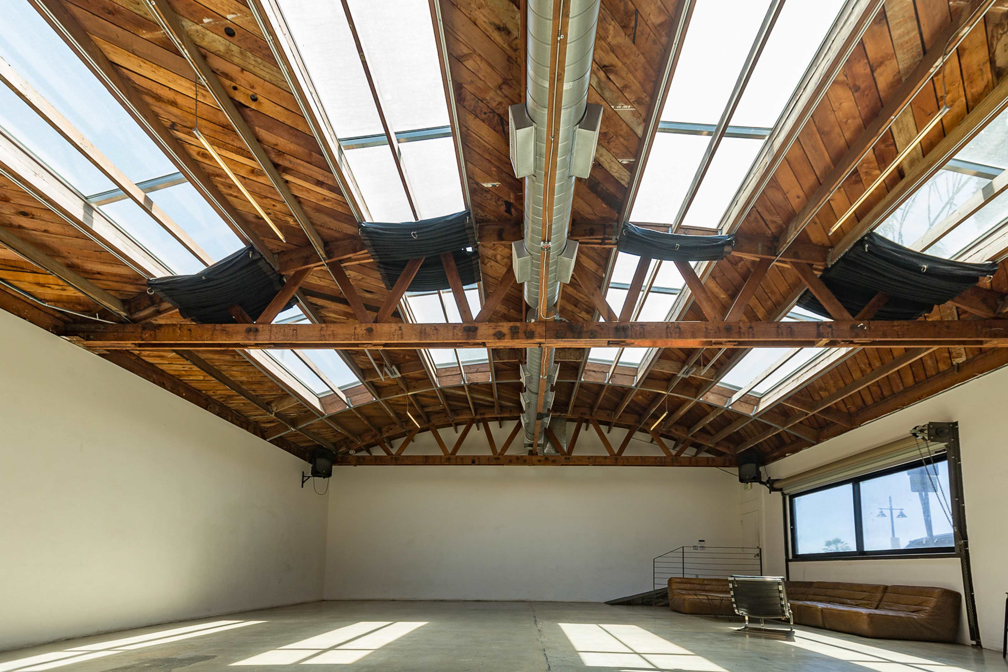 The image shows a spacious room with a wooden ceiling supported by beams and skylights allowing natural light to enter.
