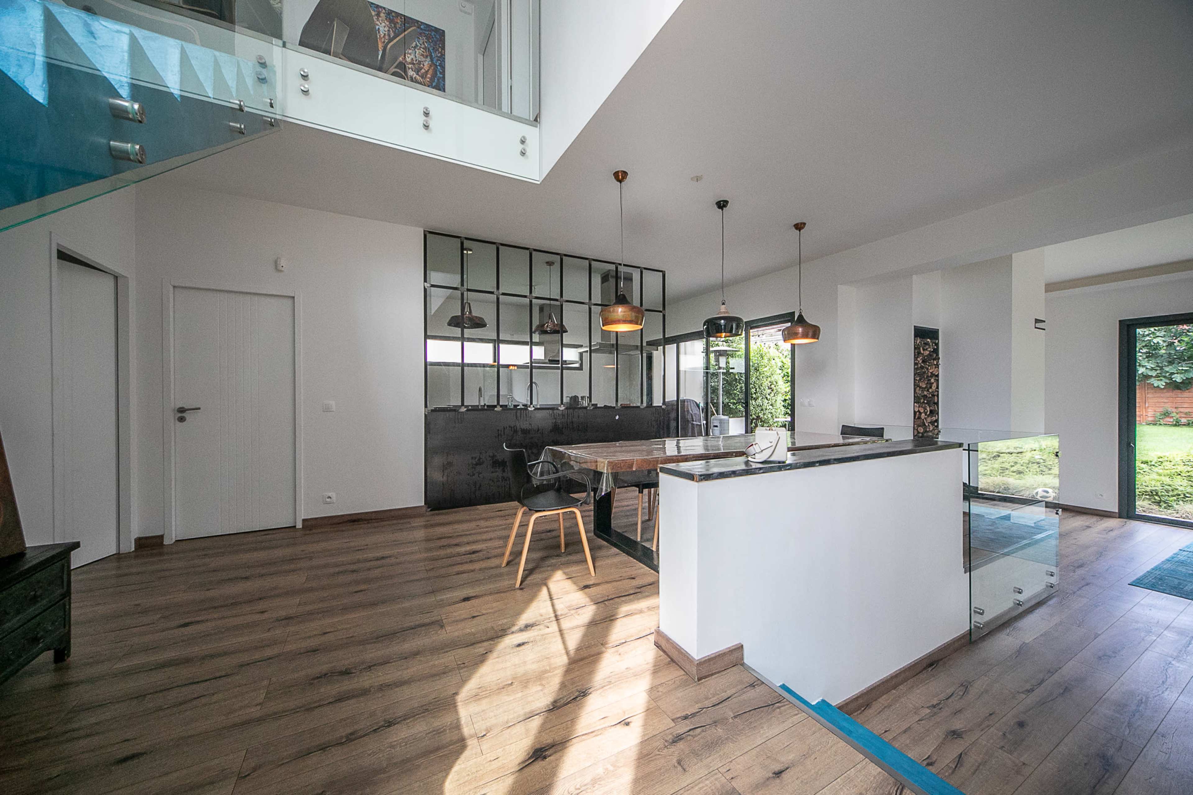A modern open-concept interior with a dining area, a kitchen with a glass counter, and large windows allowing natural light.