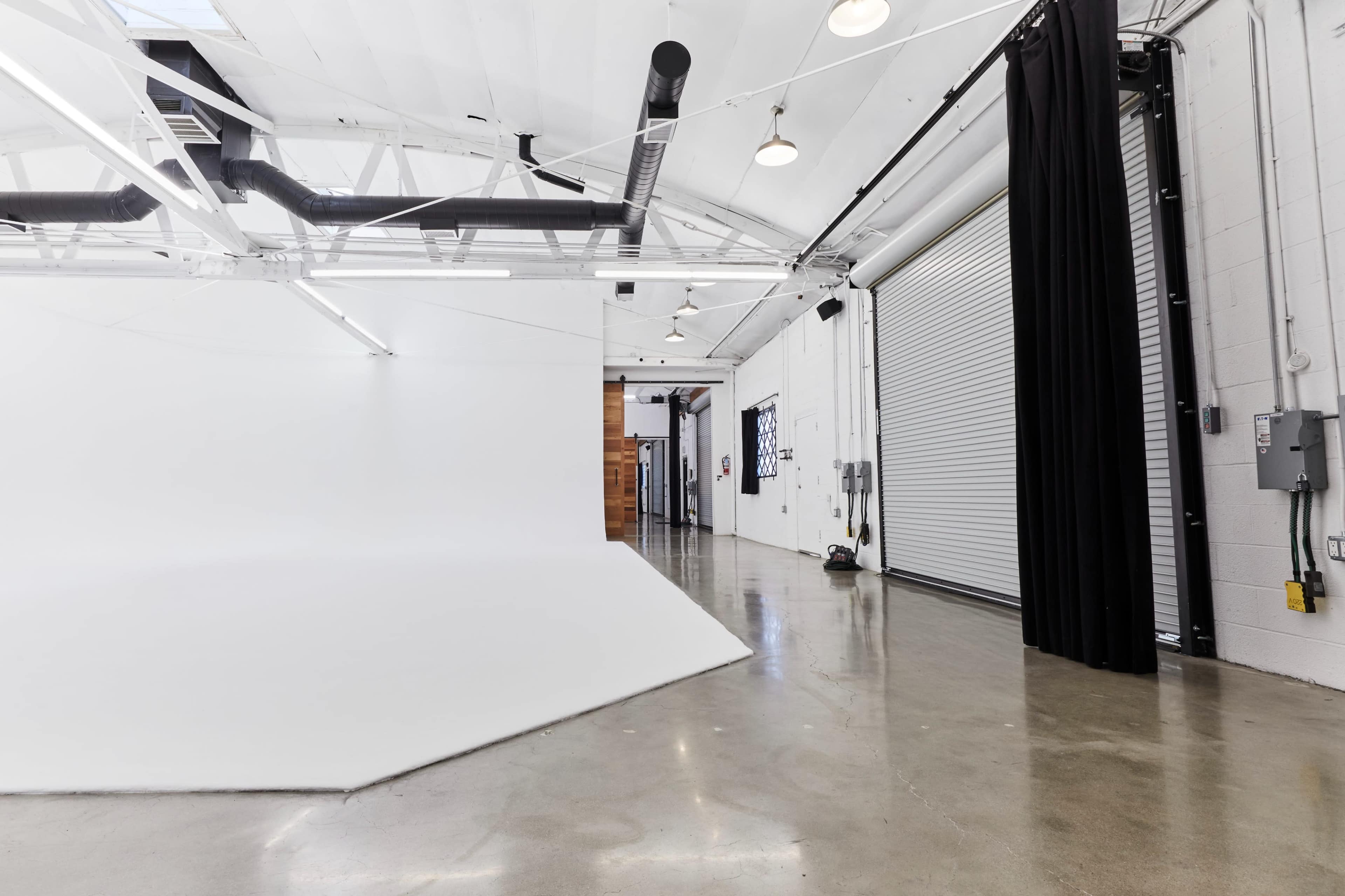 A spacious interior of a studio with white walls, a polished concrete floor, and a large roll-up door on one side.