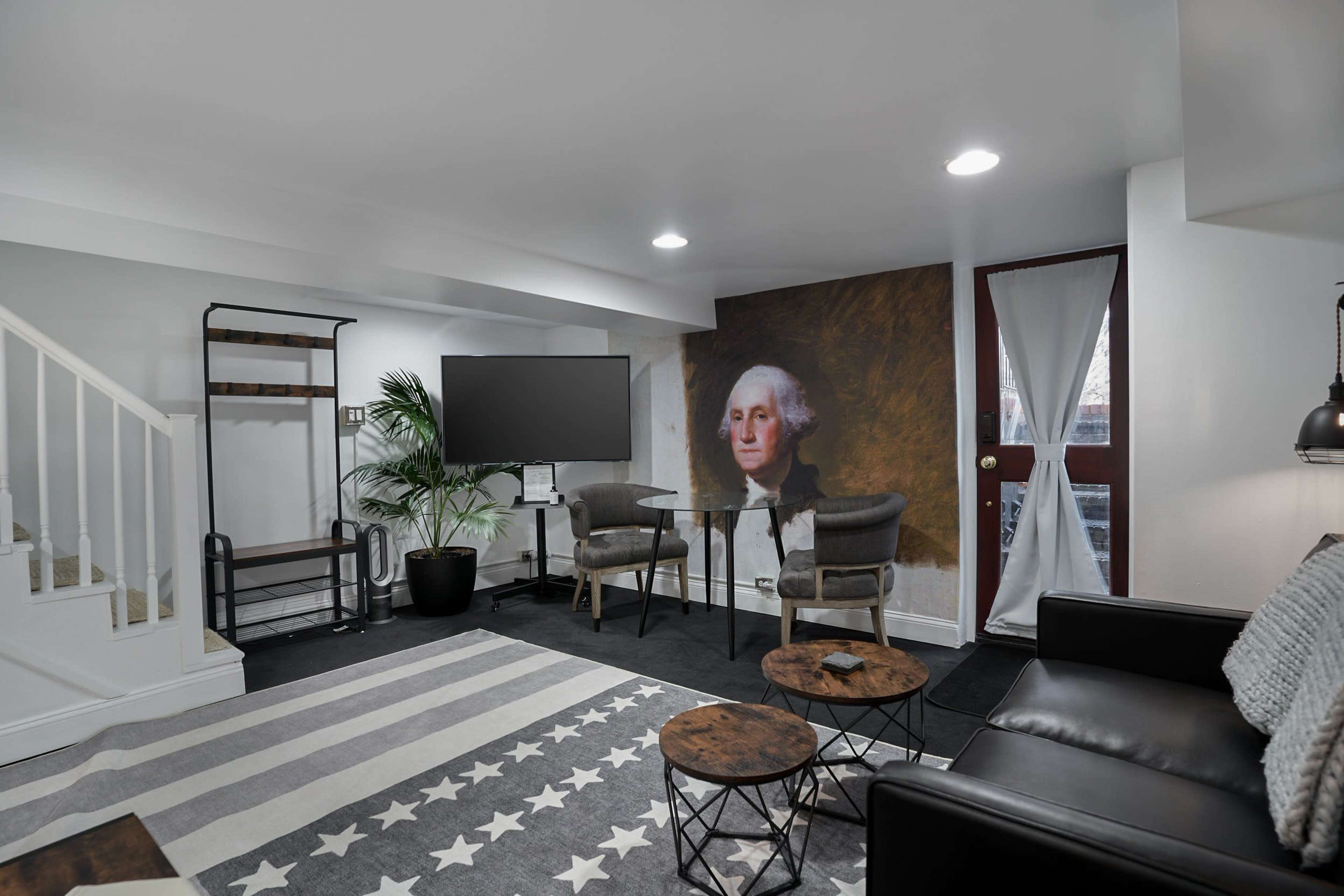 The image shows a basement sitting area with a television, a table and chairs, and a large portrait of George Washington on the wall.