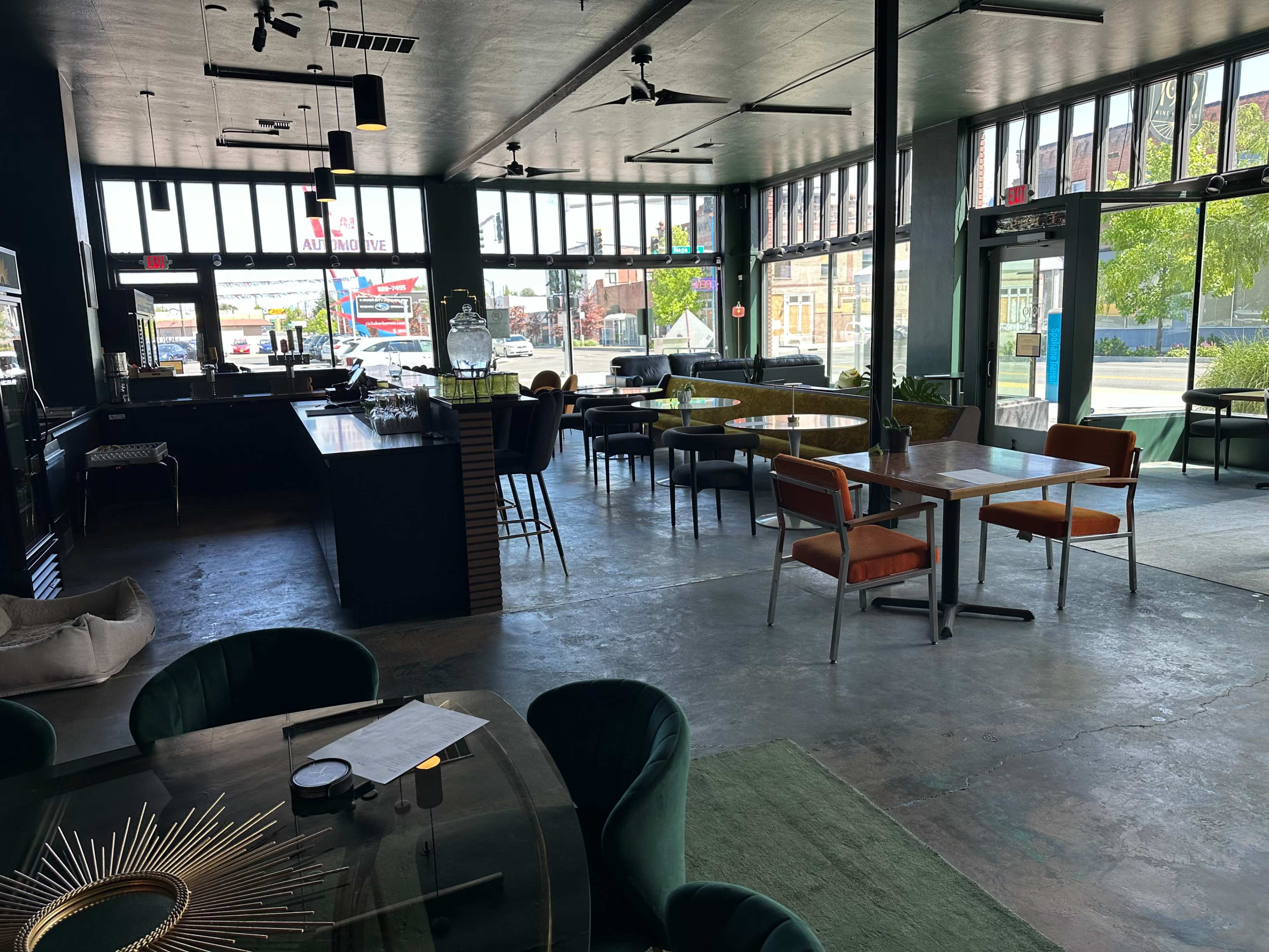 The image shows an interior of a modern restaurant with a mix of seating arrangements, large windows, and a bar area in the background.