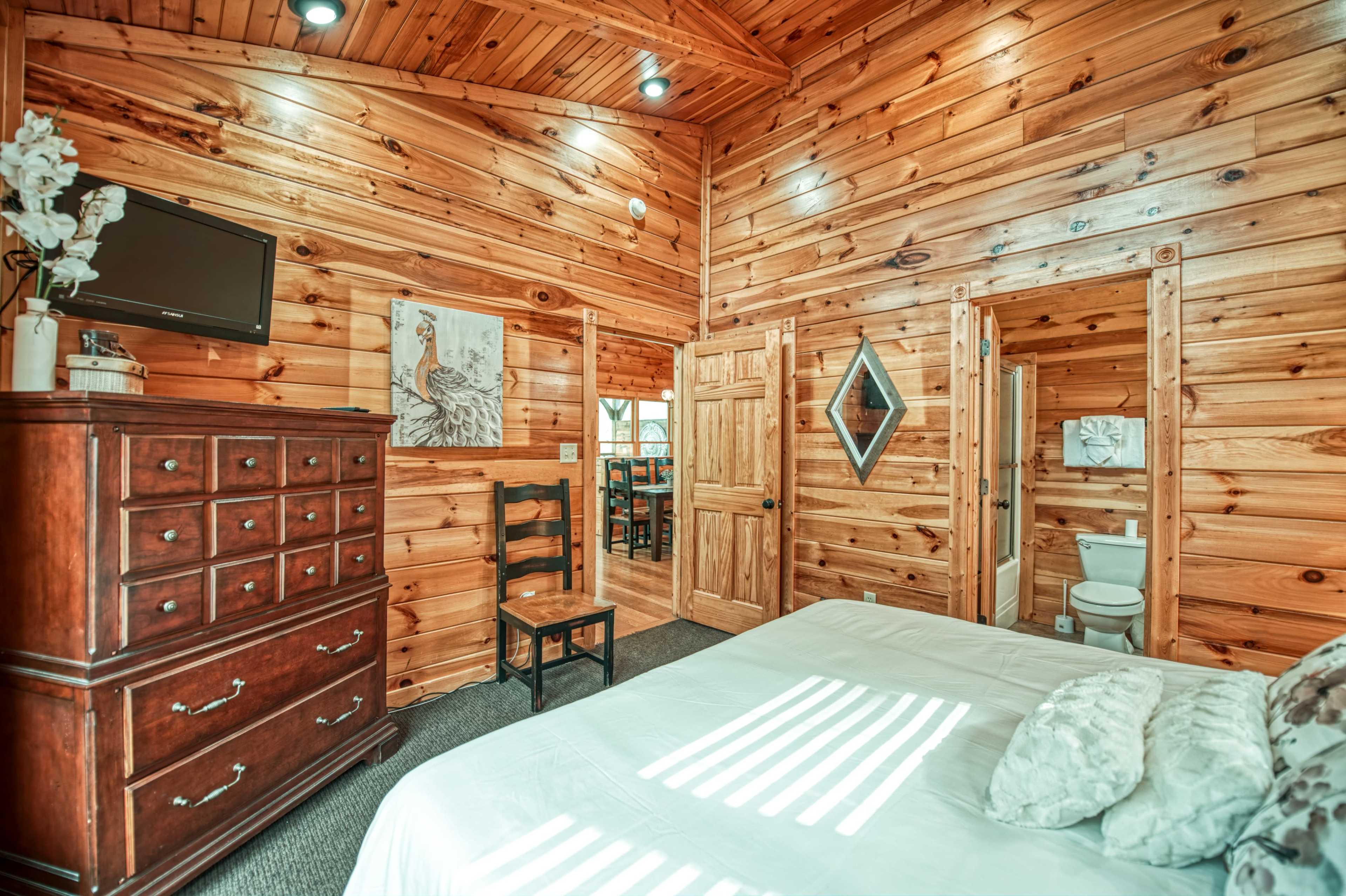 A wooden-paneled bedroom with a bed, dresser, and doorway leading to a bathroom.