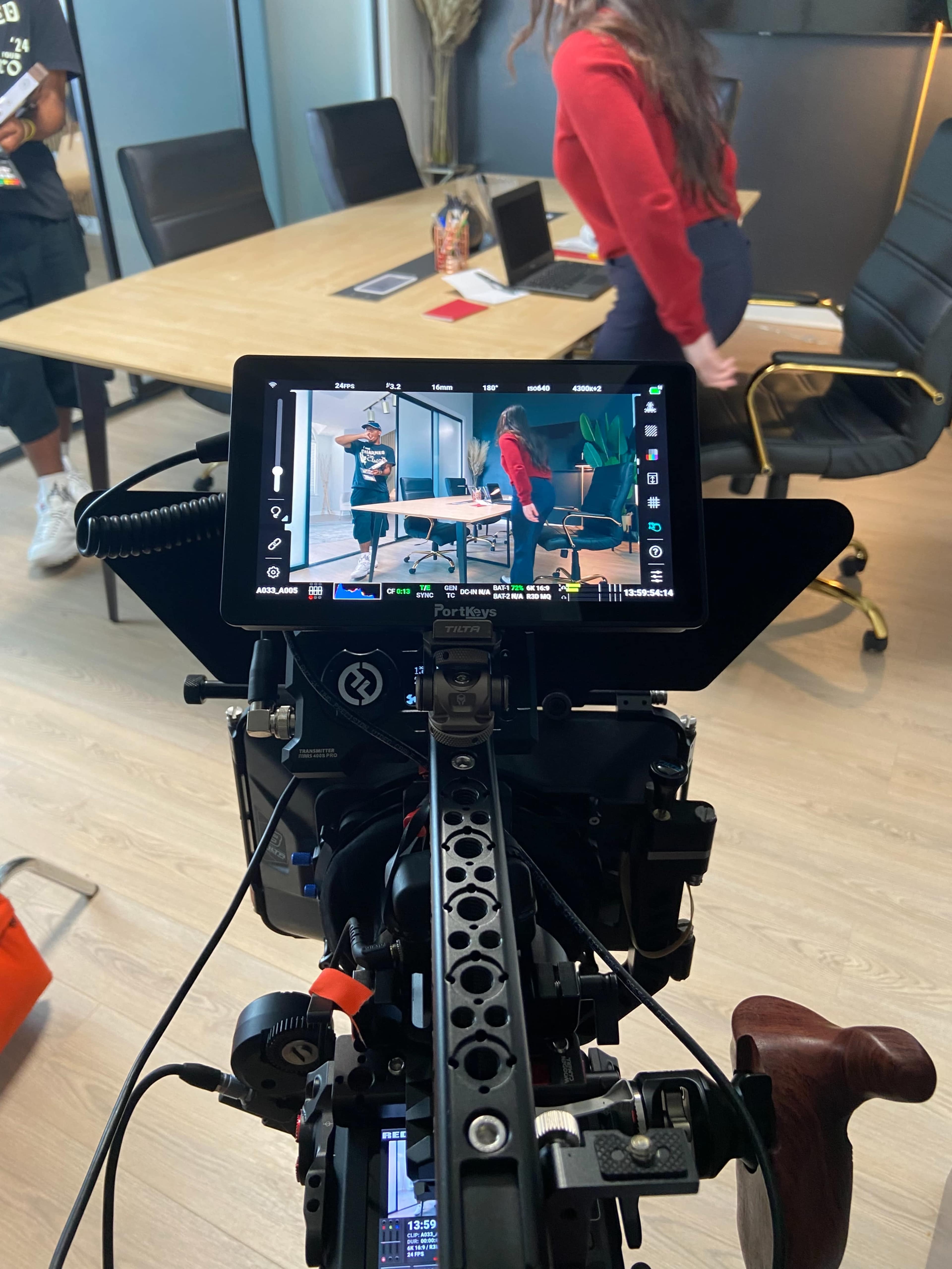 A camera is set up in a conference room, focused on two individuals engaged in a discussion near a table.