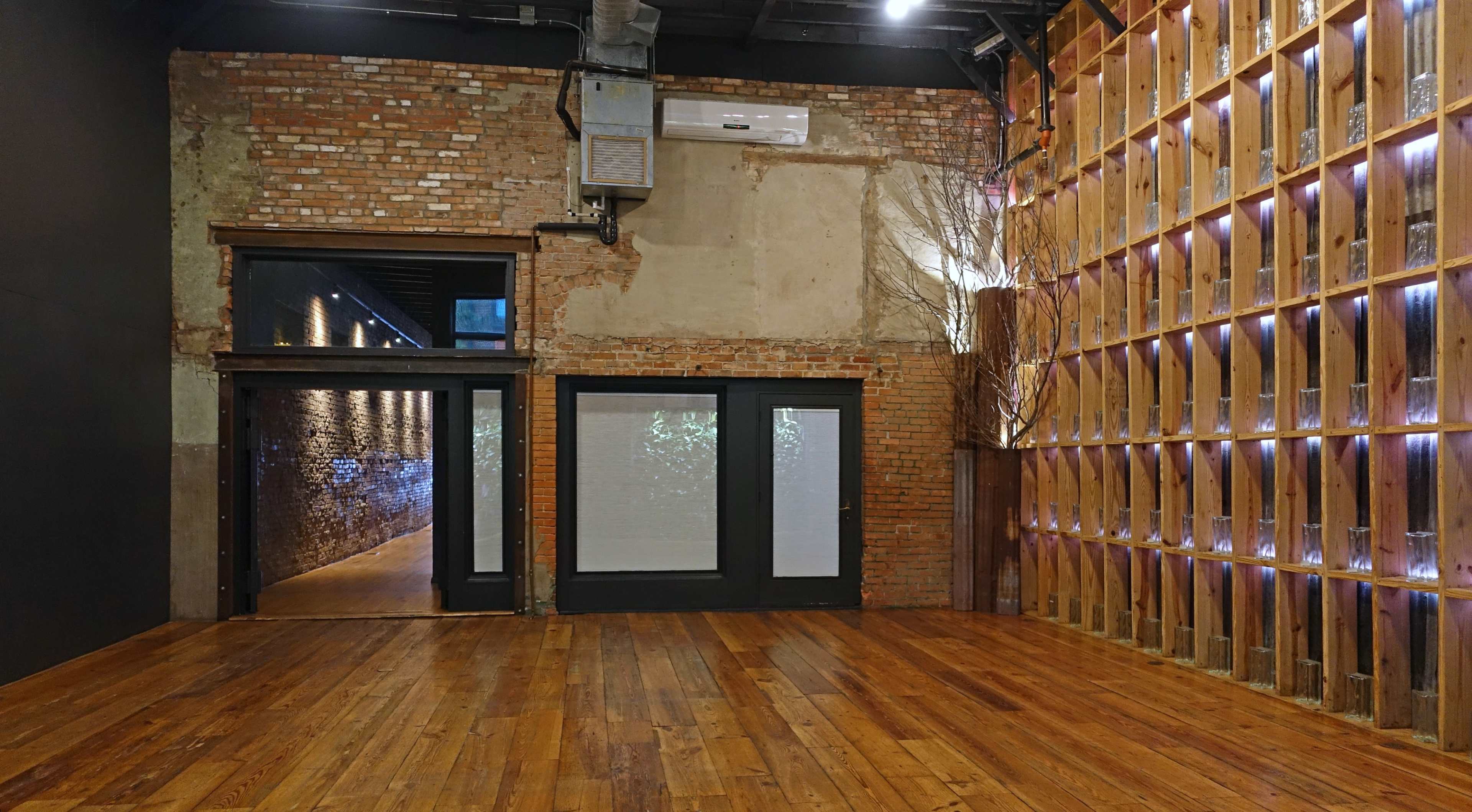 An interior space with exposed brick walls, wooden flooring, and a partition featuring a wooden framework with vertical lights.