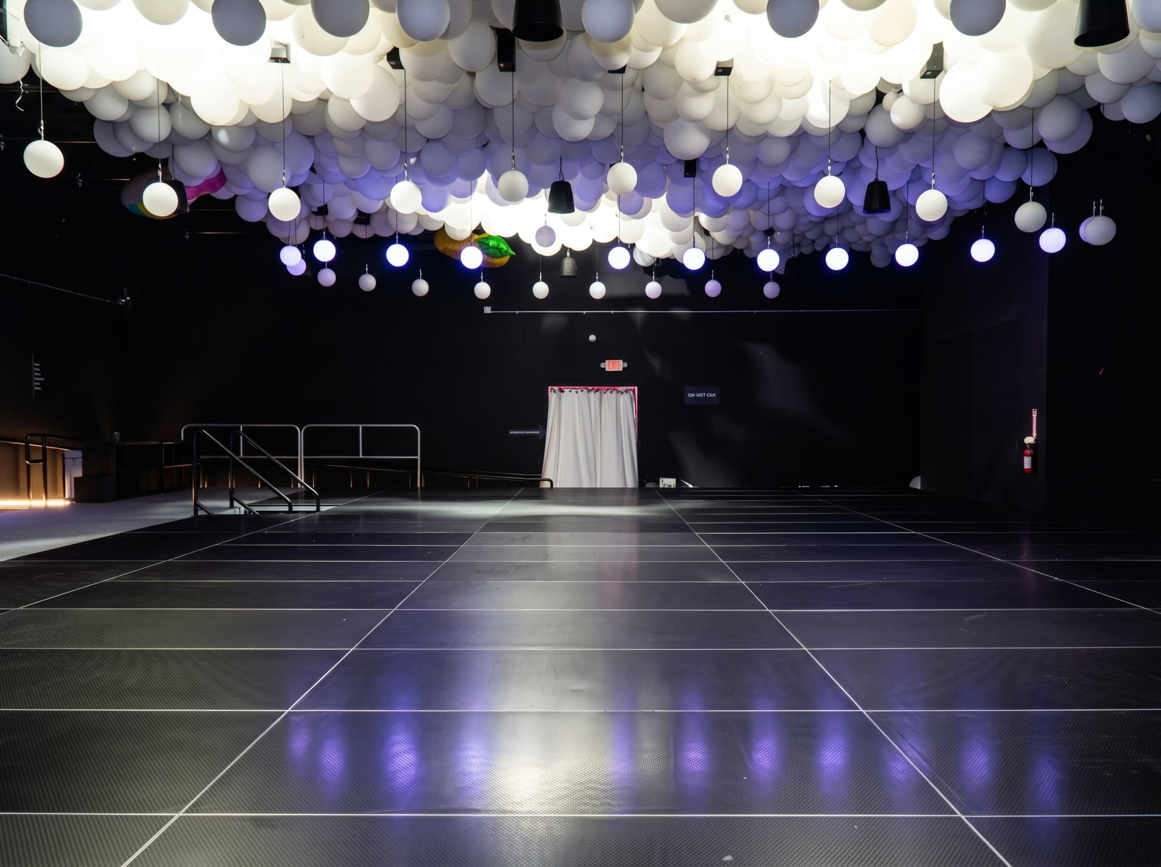 The image shows a dark venue with a spacious floor and a ceiling adorned with white spherical lights.