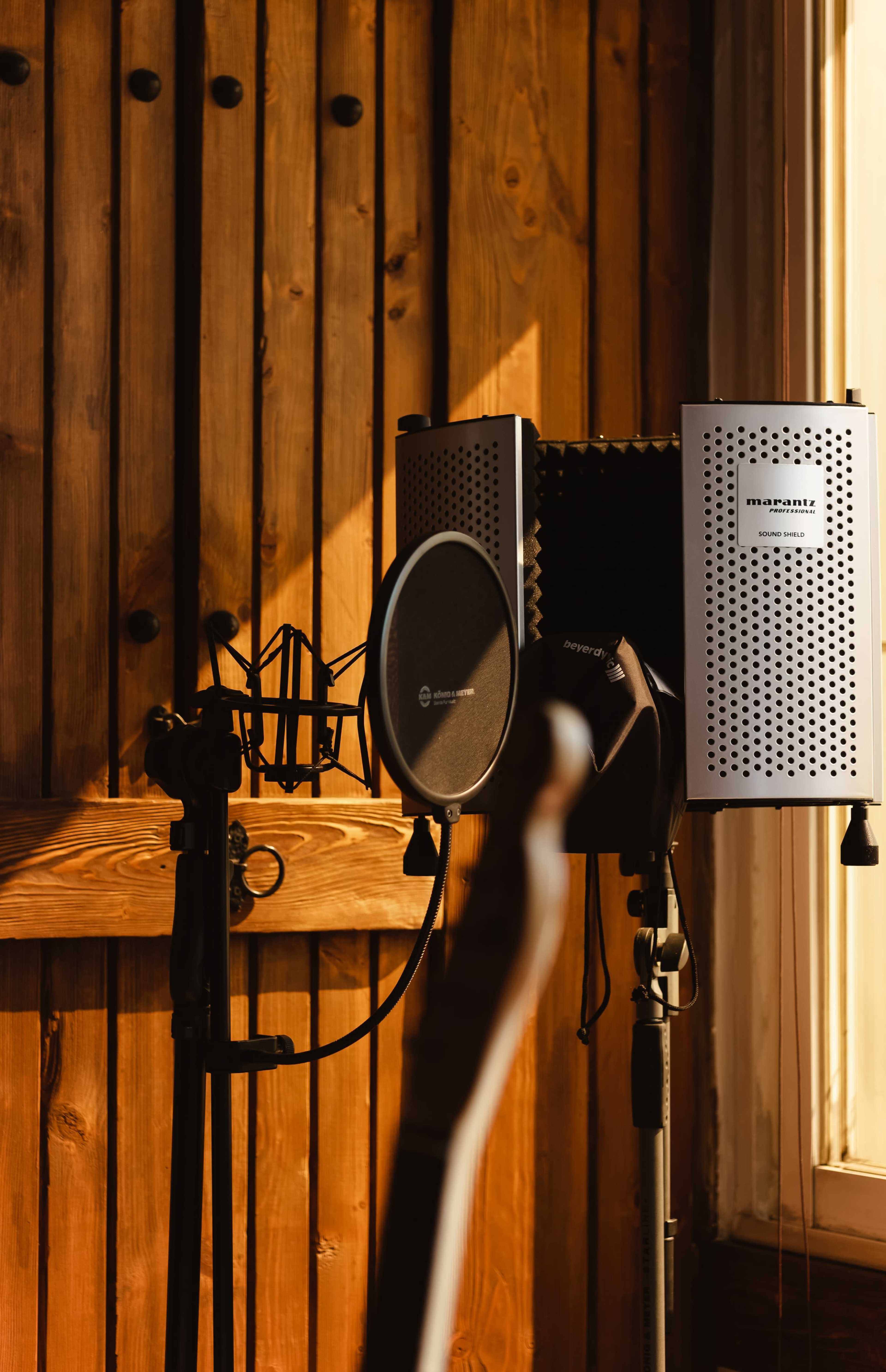 A microphone setup is positioned in front of a wooden wall, with soundproof panels and a stand for recording.