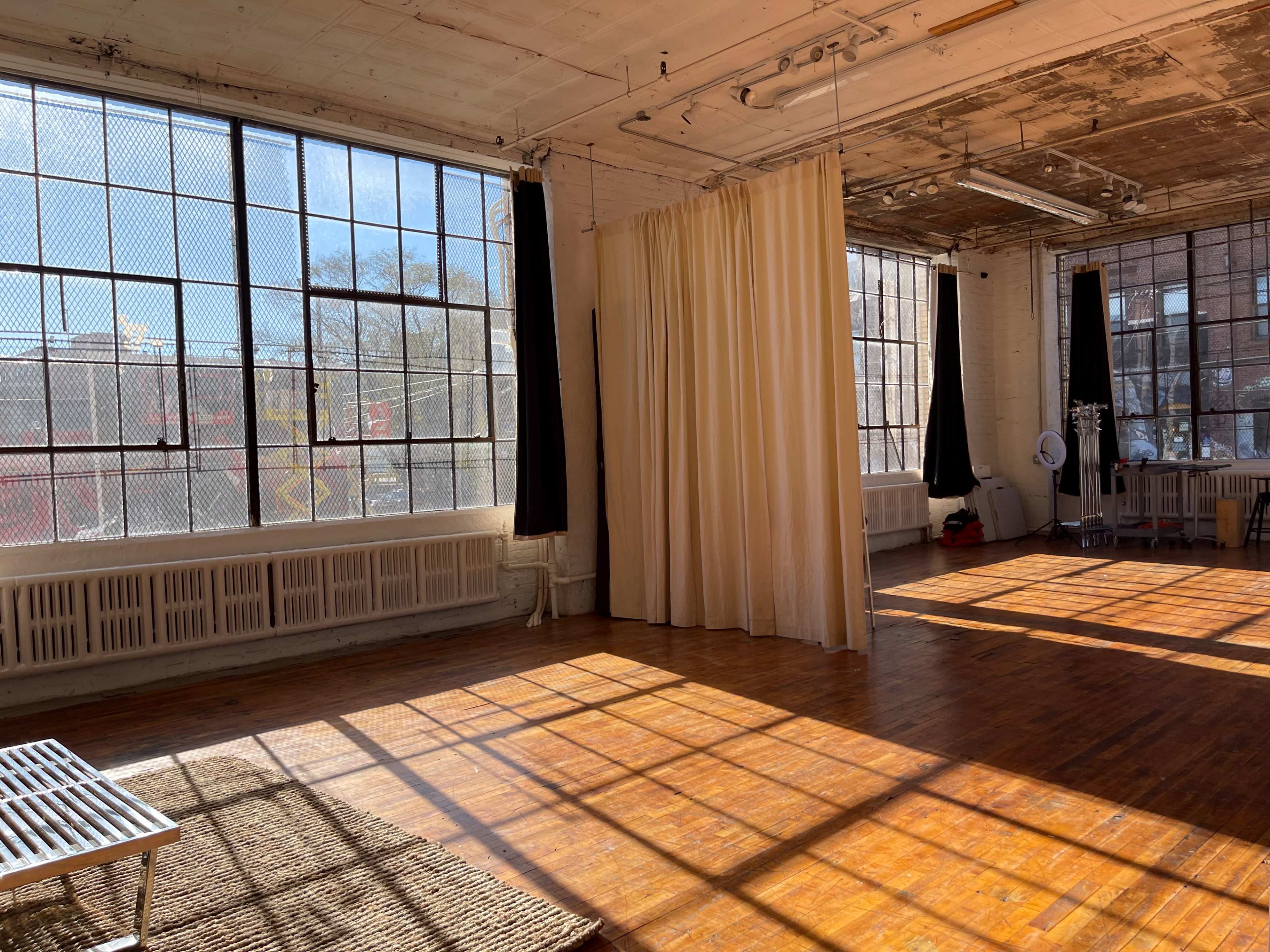 A spacious, sunlit room with large windows, wooden flooring, and white curtains.