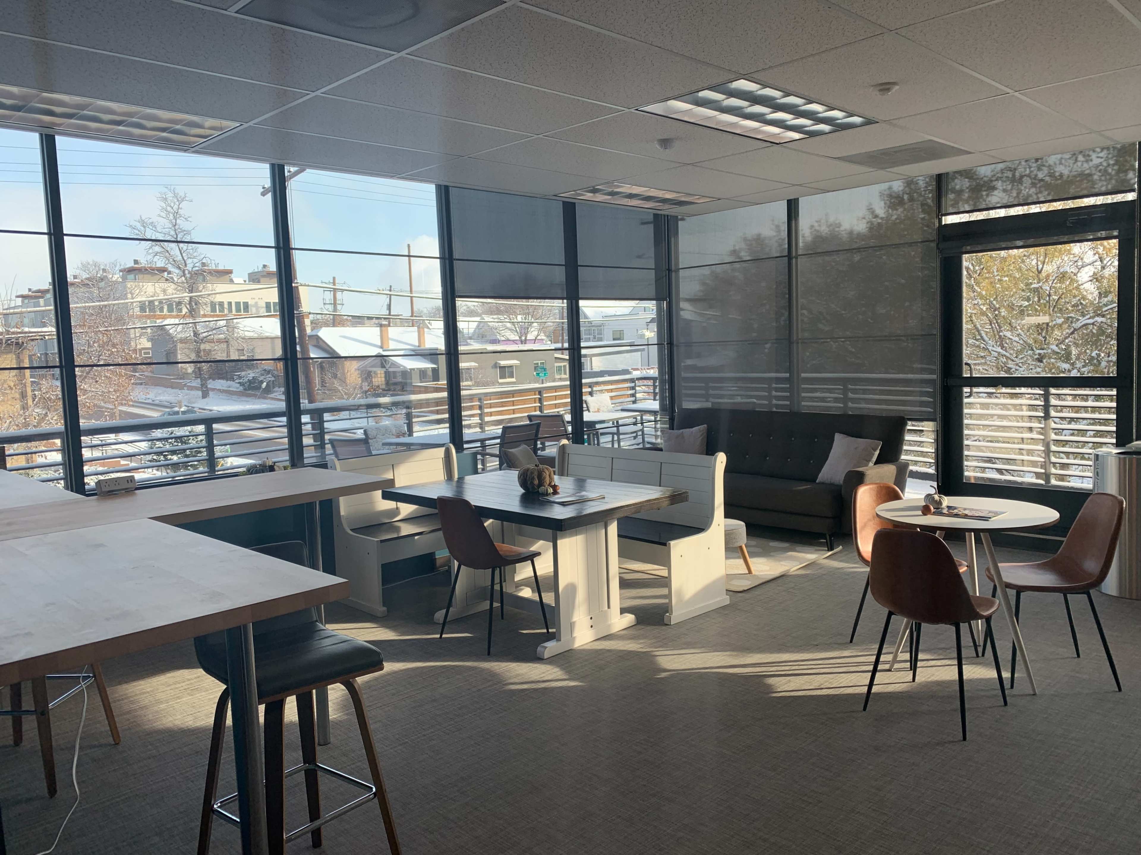 A modern office space with large windows, a mix of seating areas including tables and chairs, and a view of a snowy outdoor landscape.