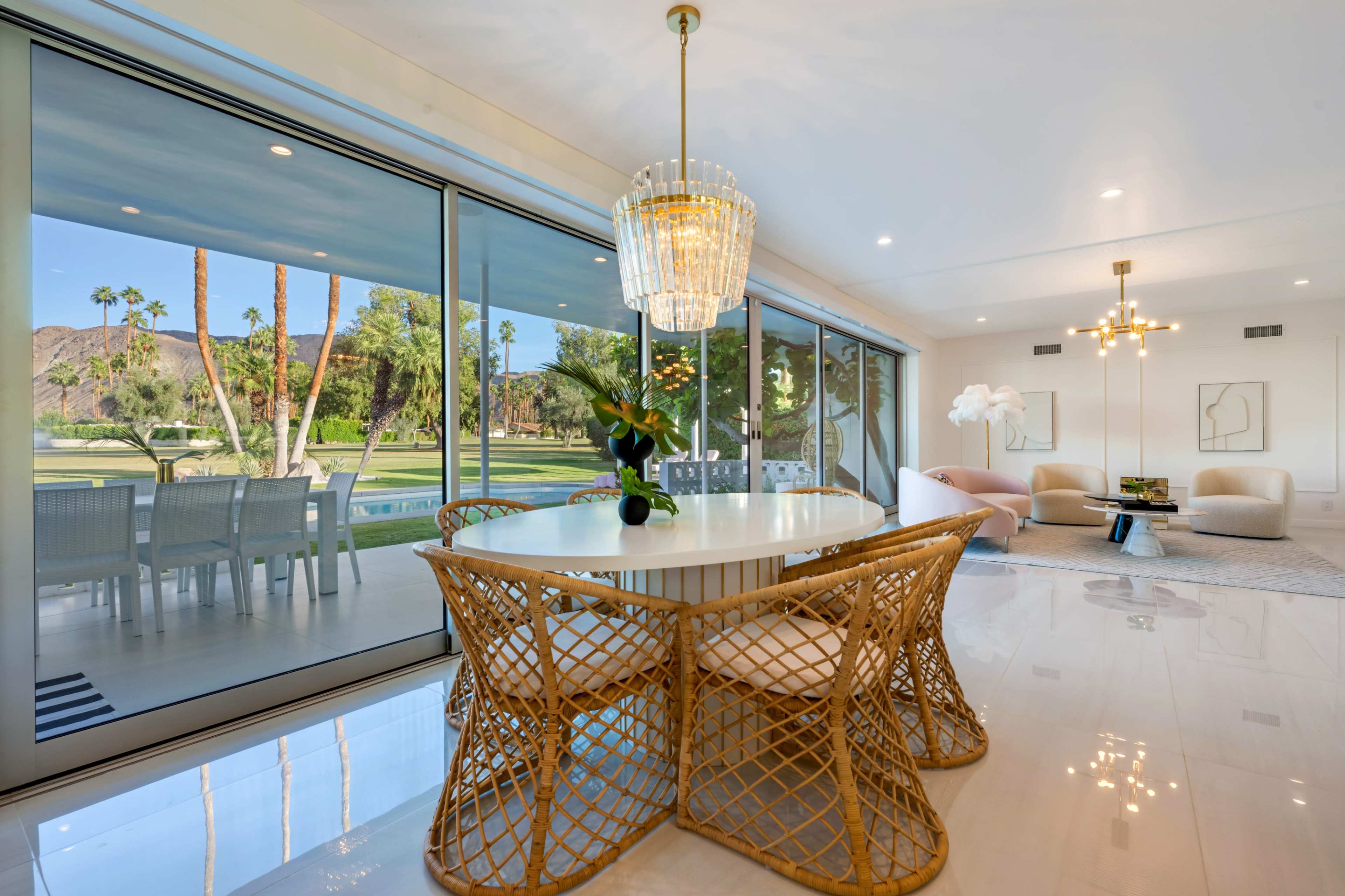 A modern dining area features a round table surrounded by four woven chairs, with large glass doors offering a view of a landscaped outdoor space.