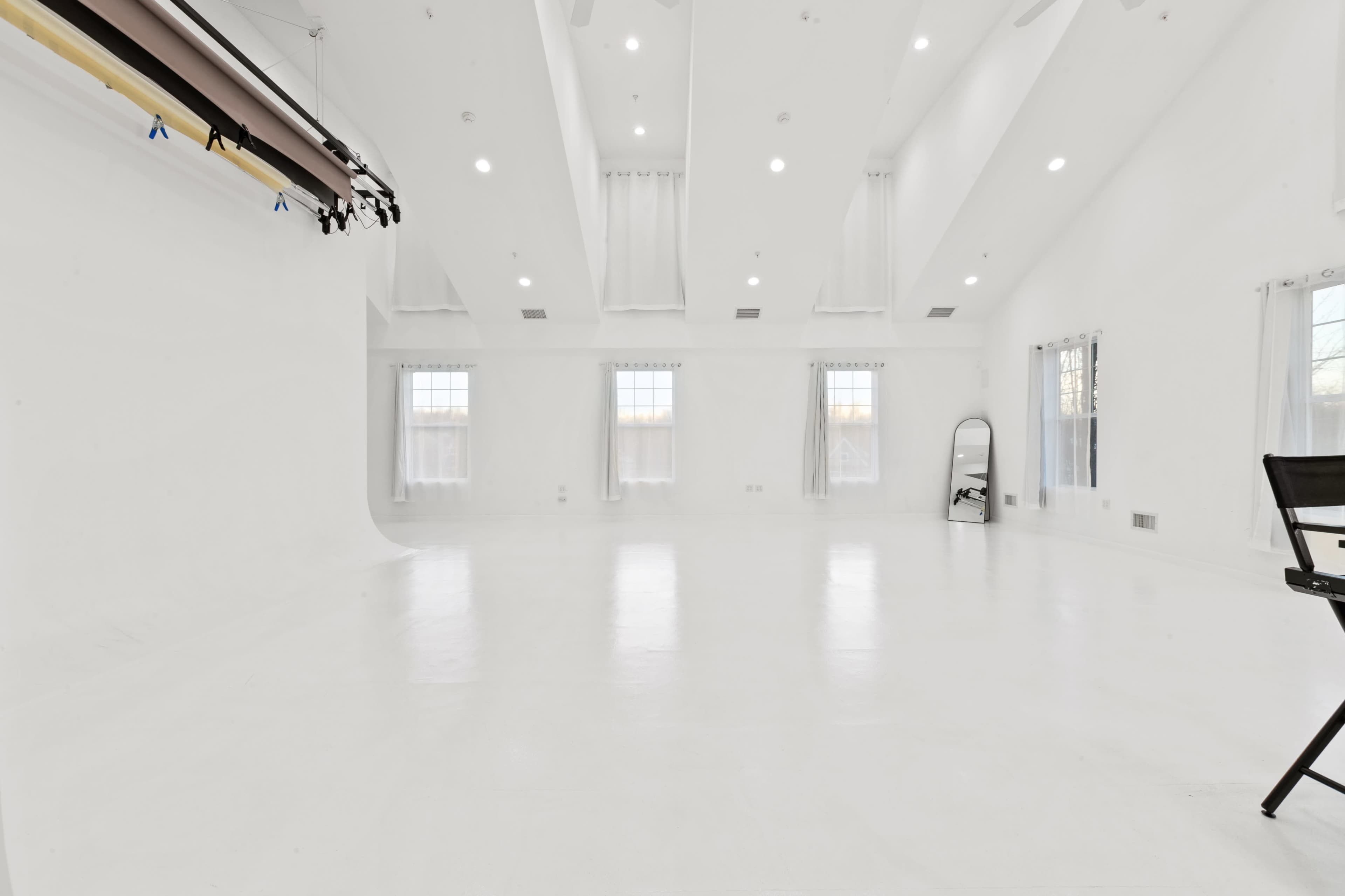 A bright, spacious studio with white walls, a polished floor, and natural light coming through large windows.