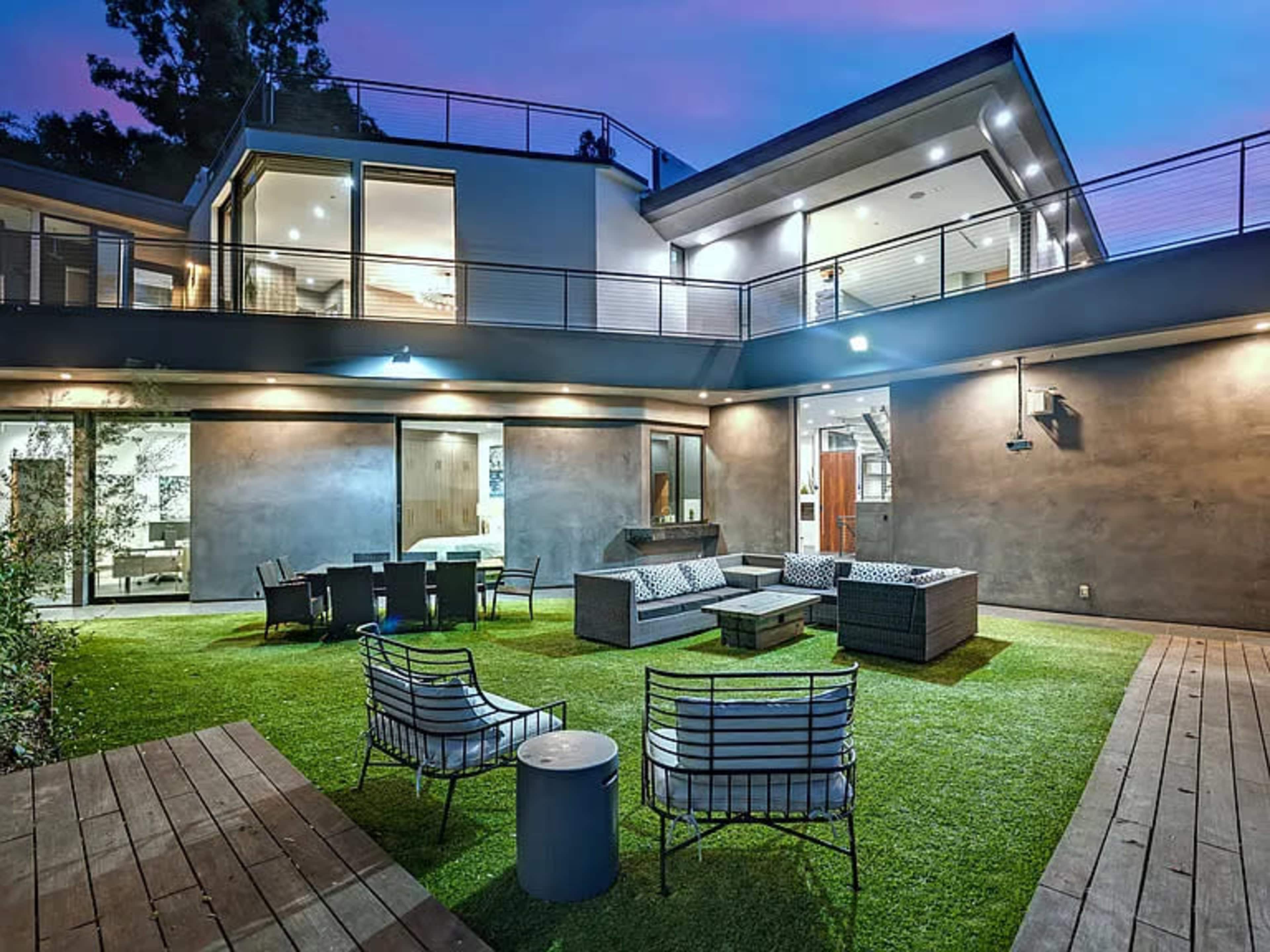 A modern outdoor living space features a grassy area with seating arrangements and a dining table surrounded by a contemporary home.