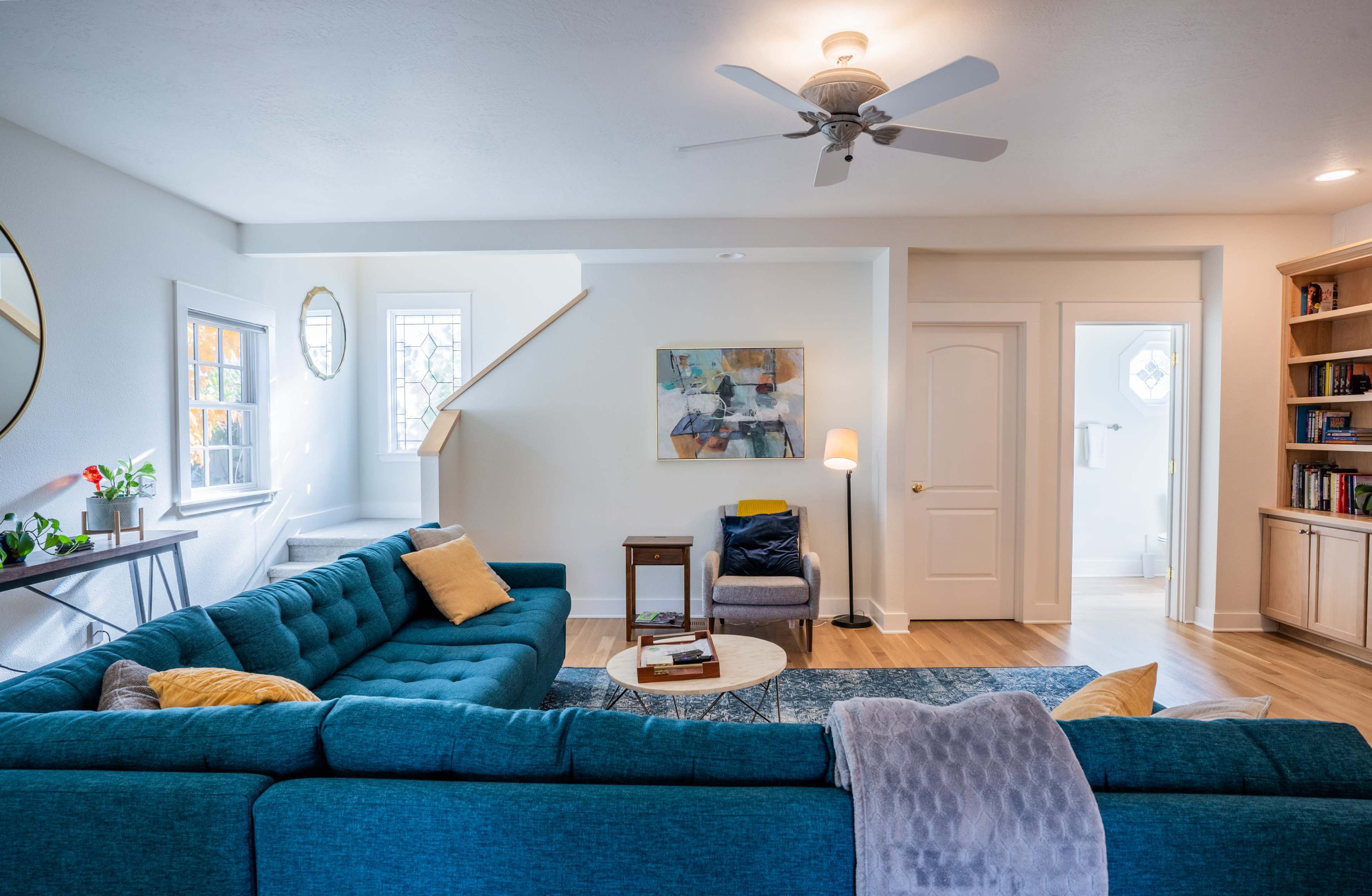 A modern living room features a large blue sectional sofa, a coffee table, and a staircase leading to an upper level.