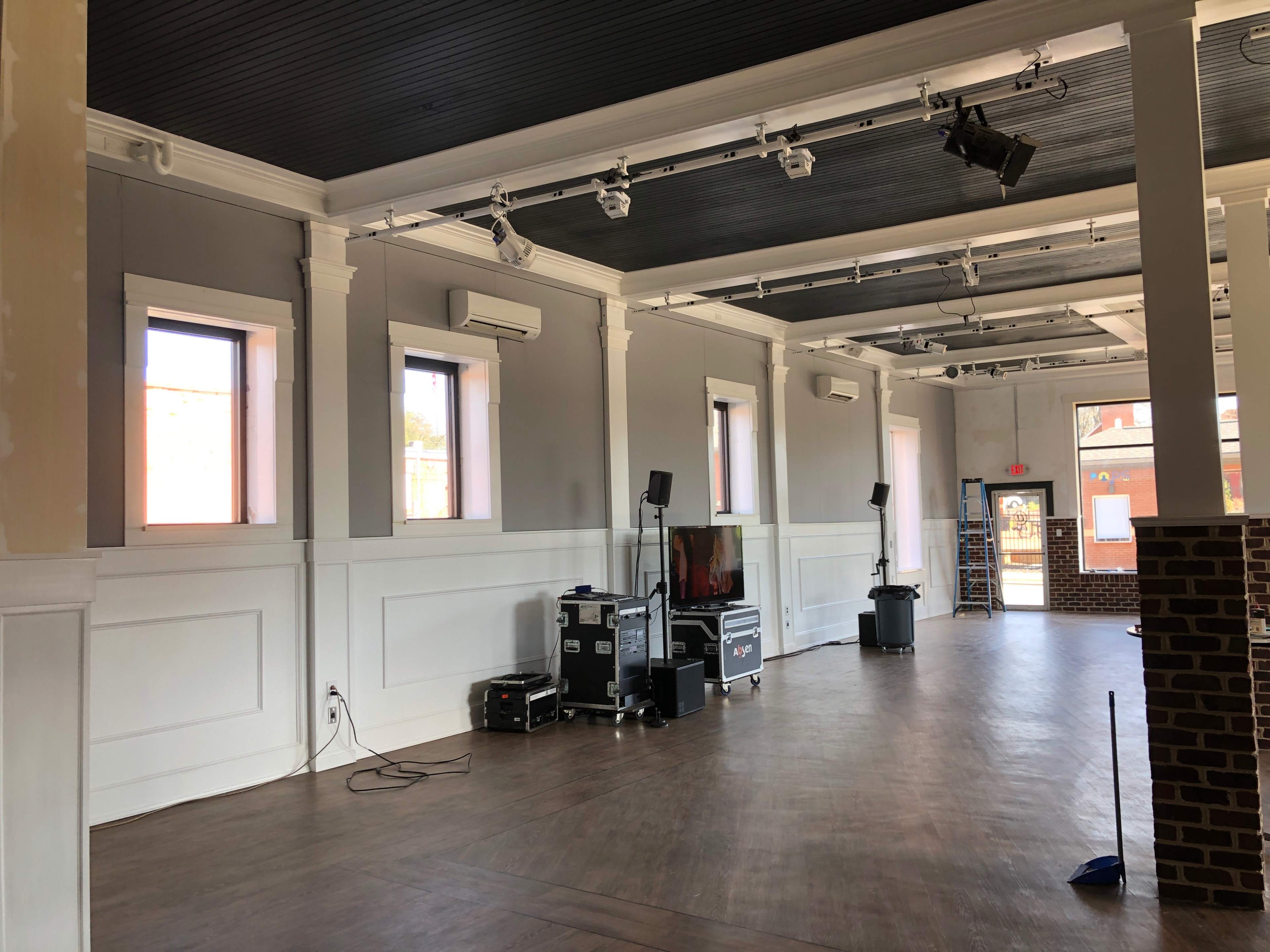 A spacious interior with gray walls, large windows, and sound equipment set up near a brick column.