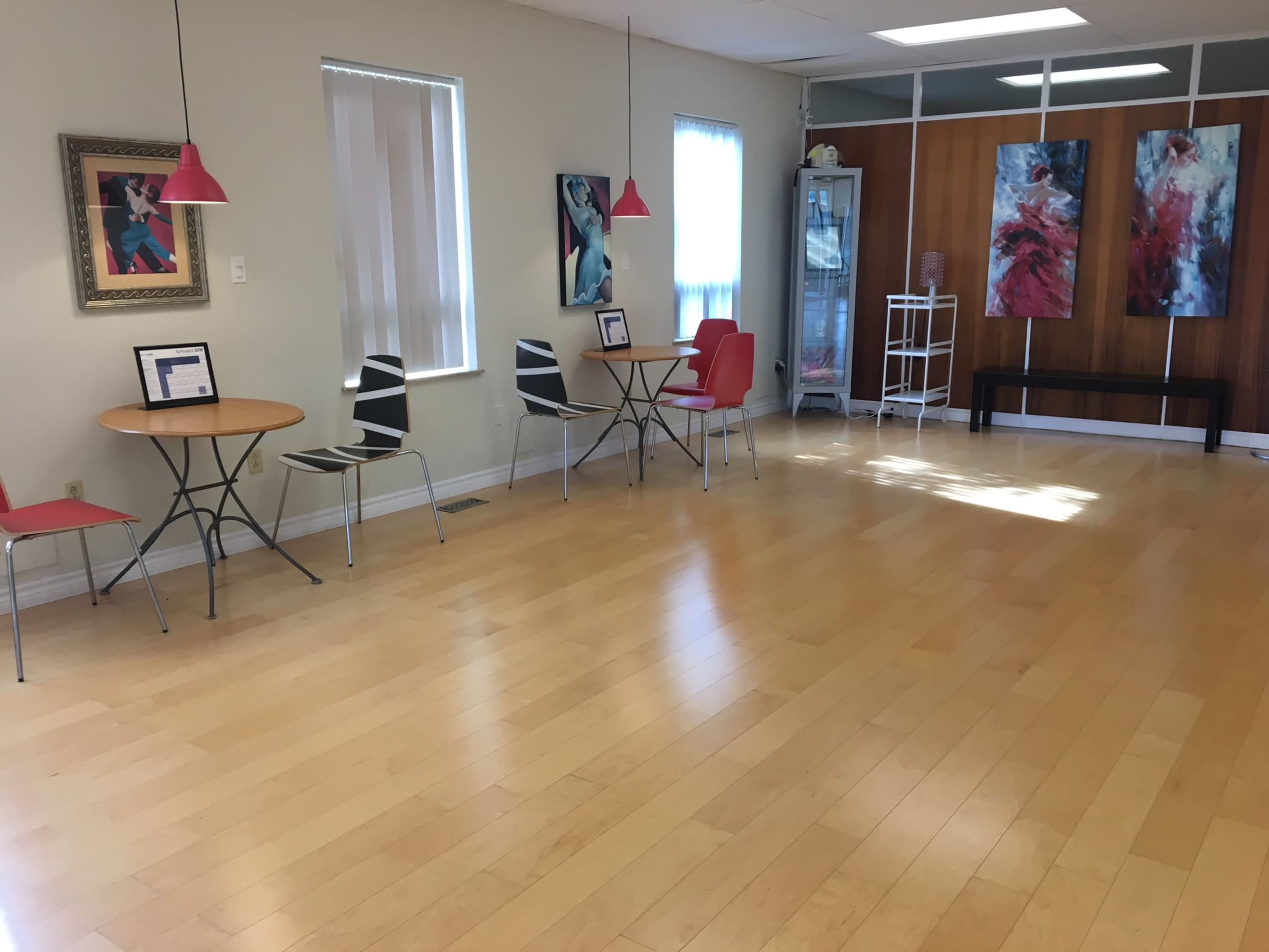 A bright room with wooden floors, two tables surrounded by chairs, and colorful artwork displayed on the walls.