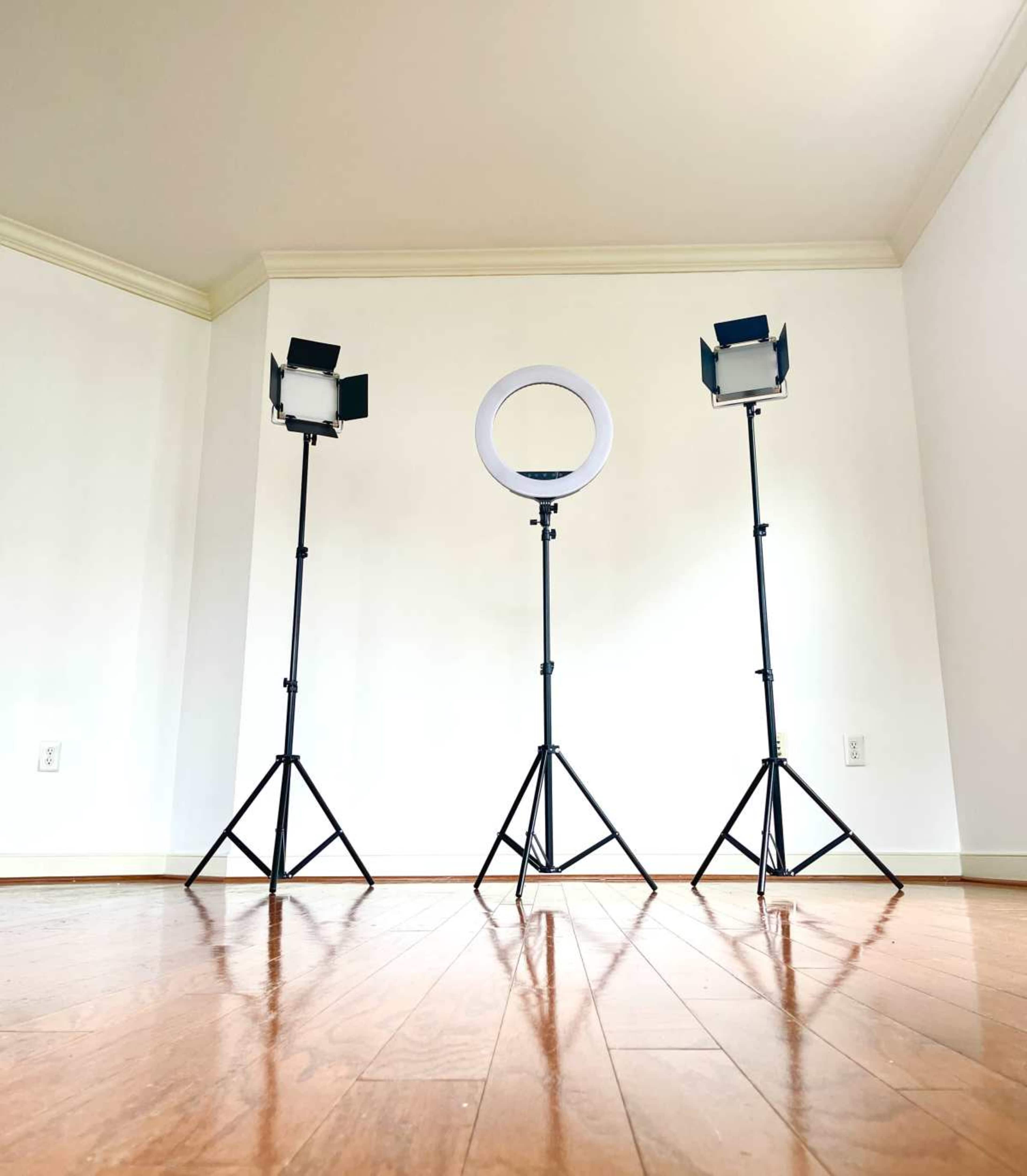 The image shows three lighting equipment stands set up on a wooden floor in an empty room with white walls.