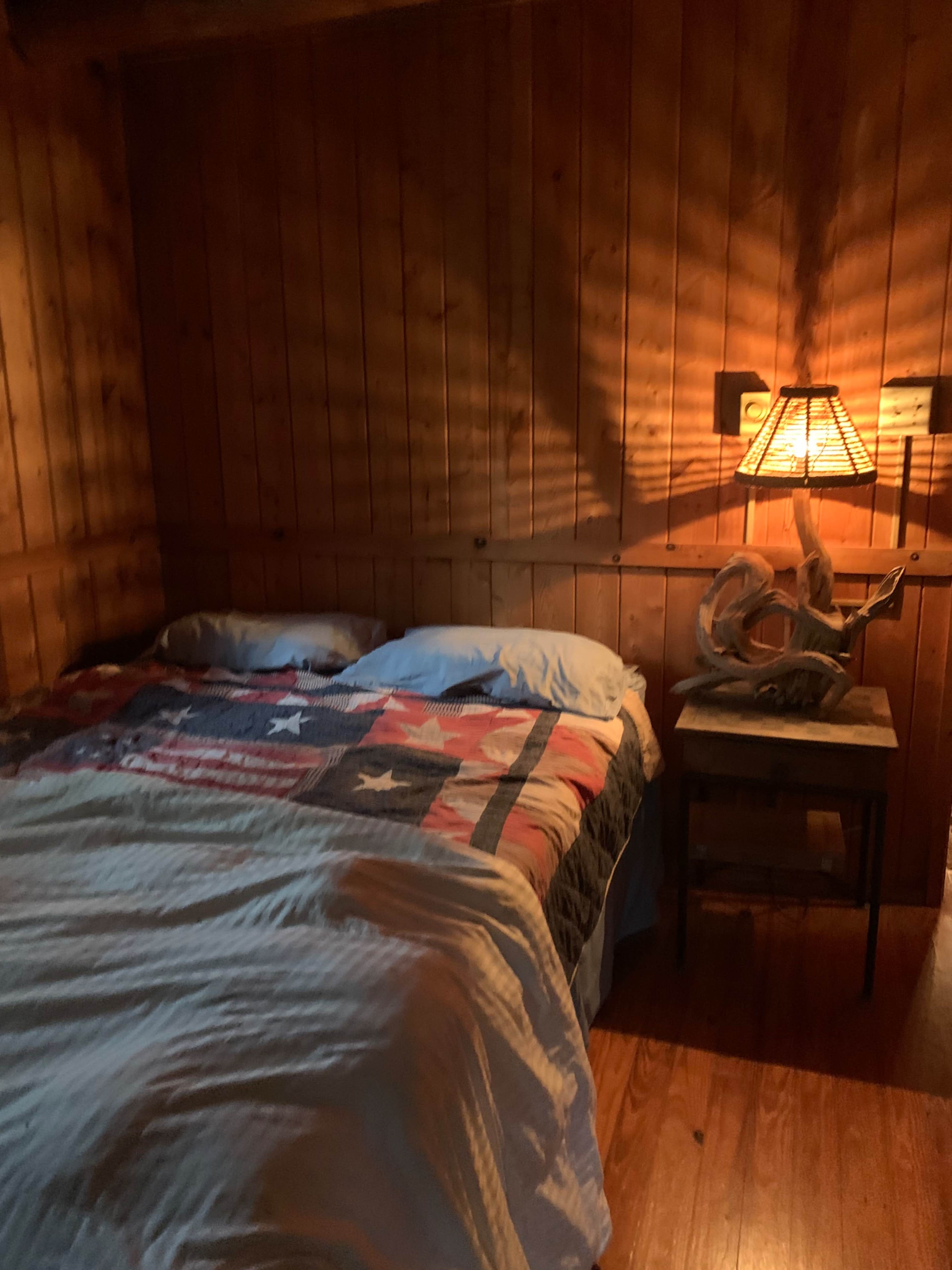 A rustic bedroom with a wooden wall, a bed covered with a star-patterned quilt, and a bedside table with a lamp and decorative antlers.