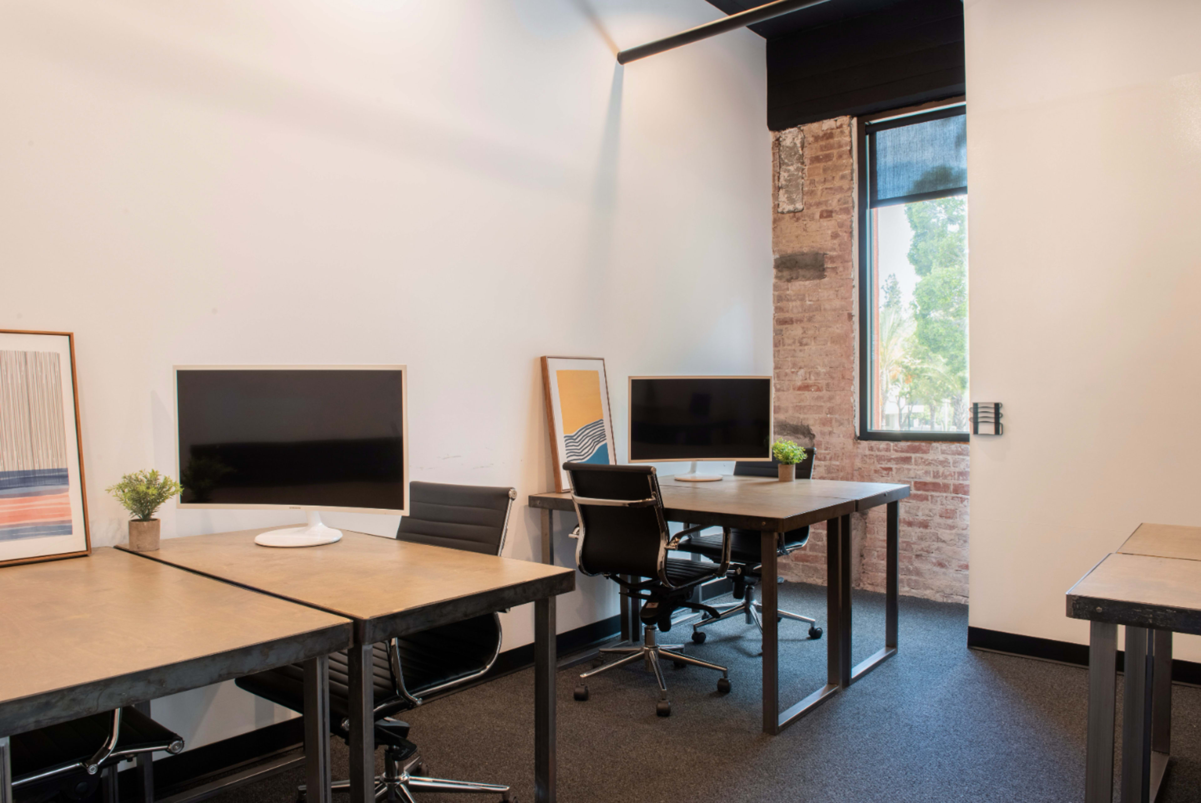The image shows a modern office space with two desks, each equipped with a monitor, and a window providing natural light.