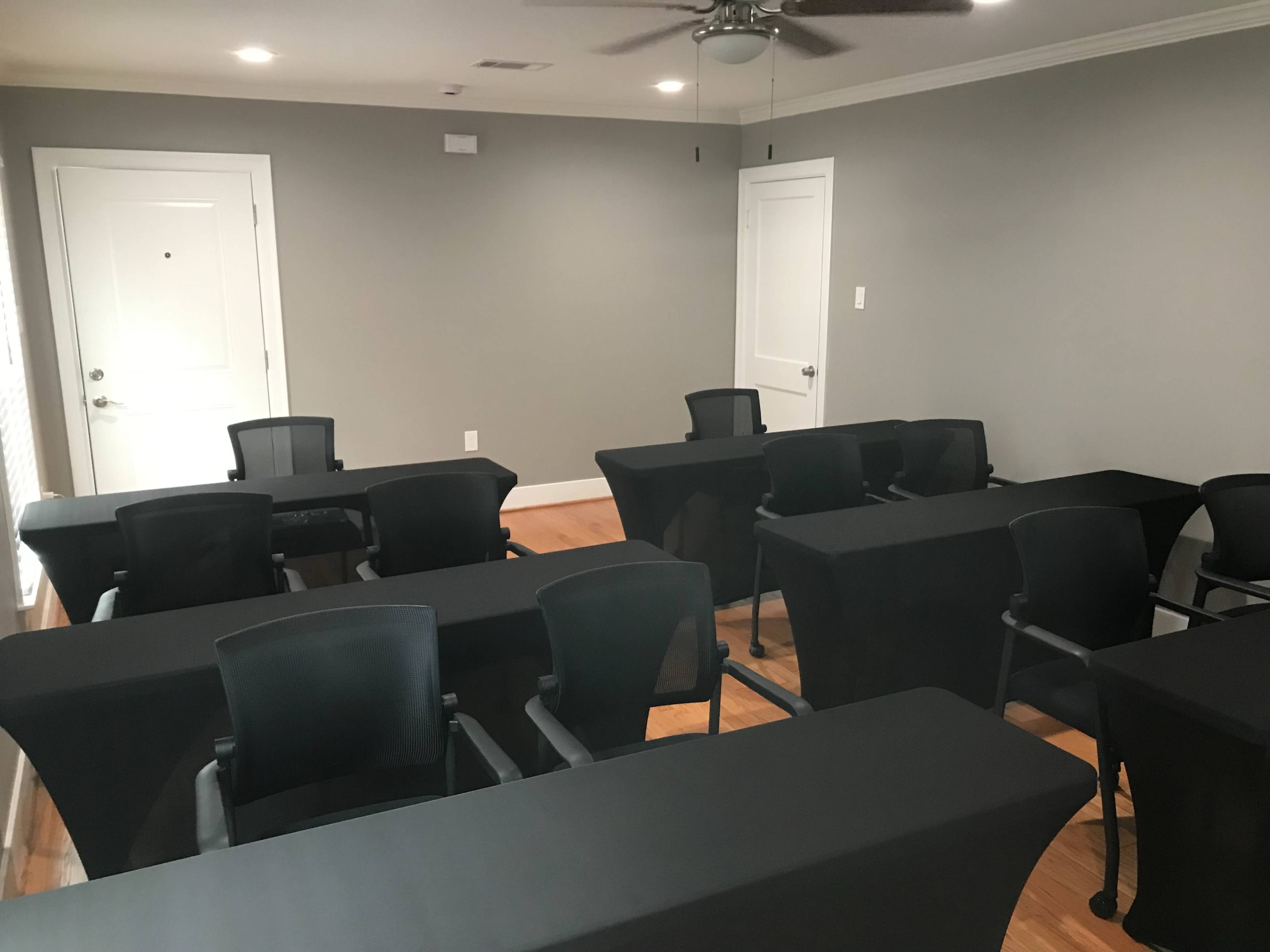 The image shows a meeting room with several black tables and chairs arranged facing a wall.