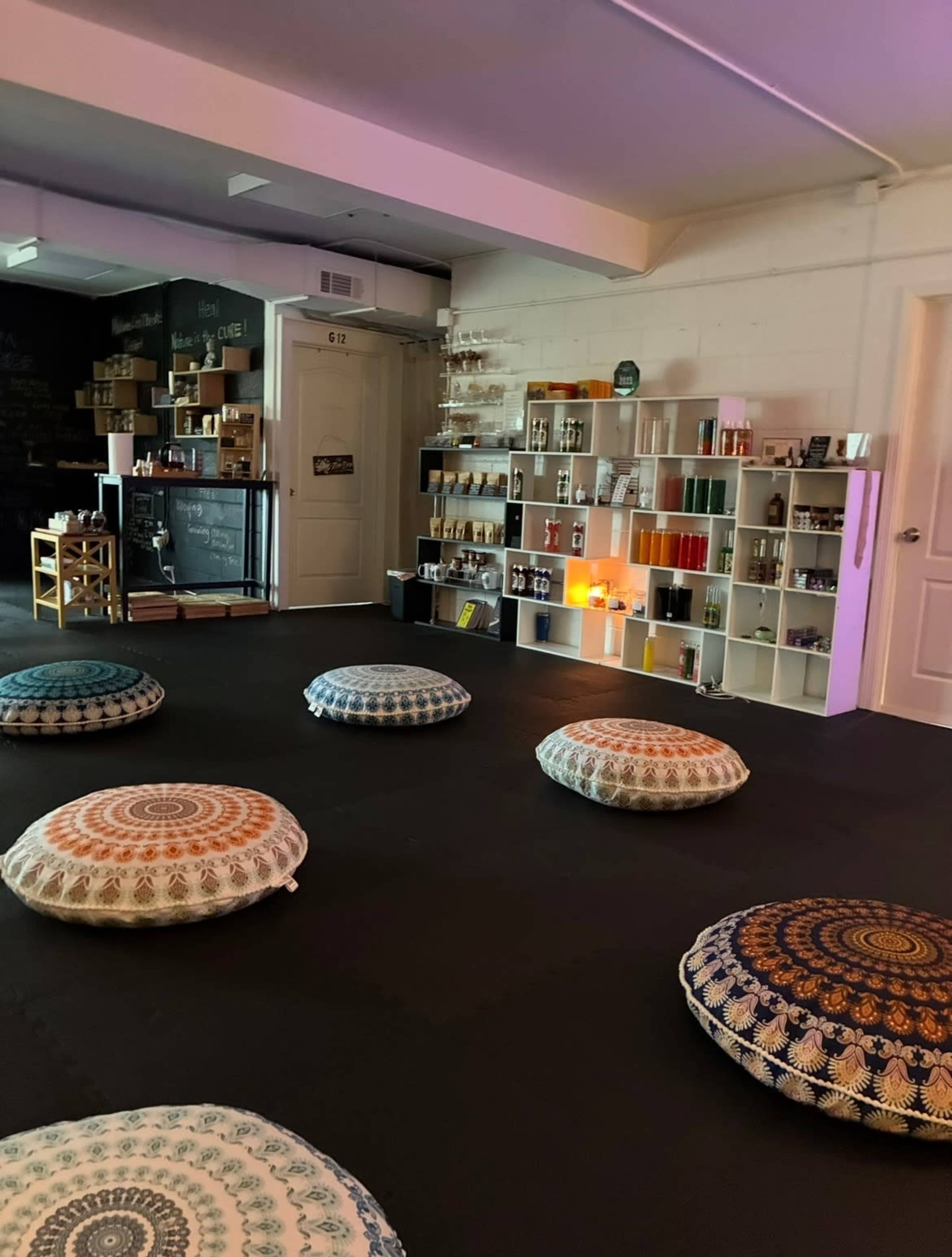 The image shows a wellness space with circular floor cushions arranged on a black mat and shelves displaying various products against a wall.