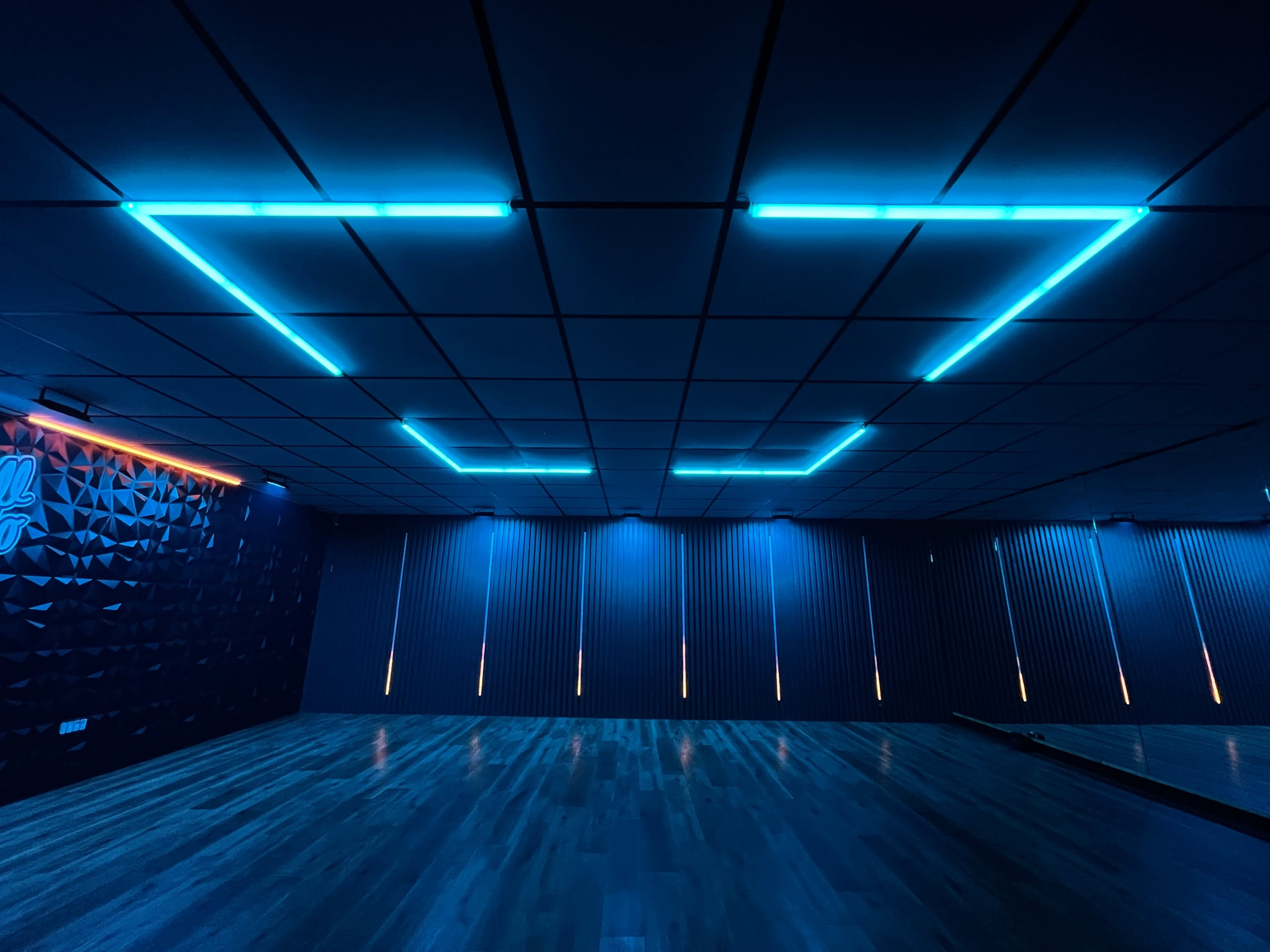 A dimly lit room with blue neon lighting along the ceiling and vertical wall accents, featuring a polished wooden floor.