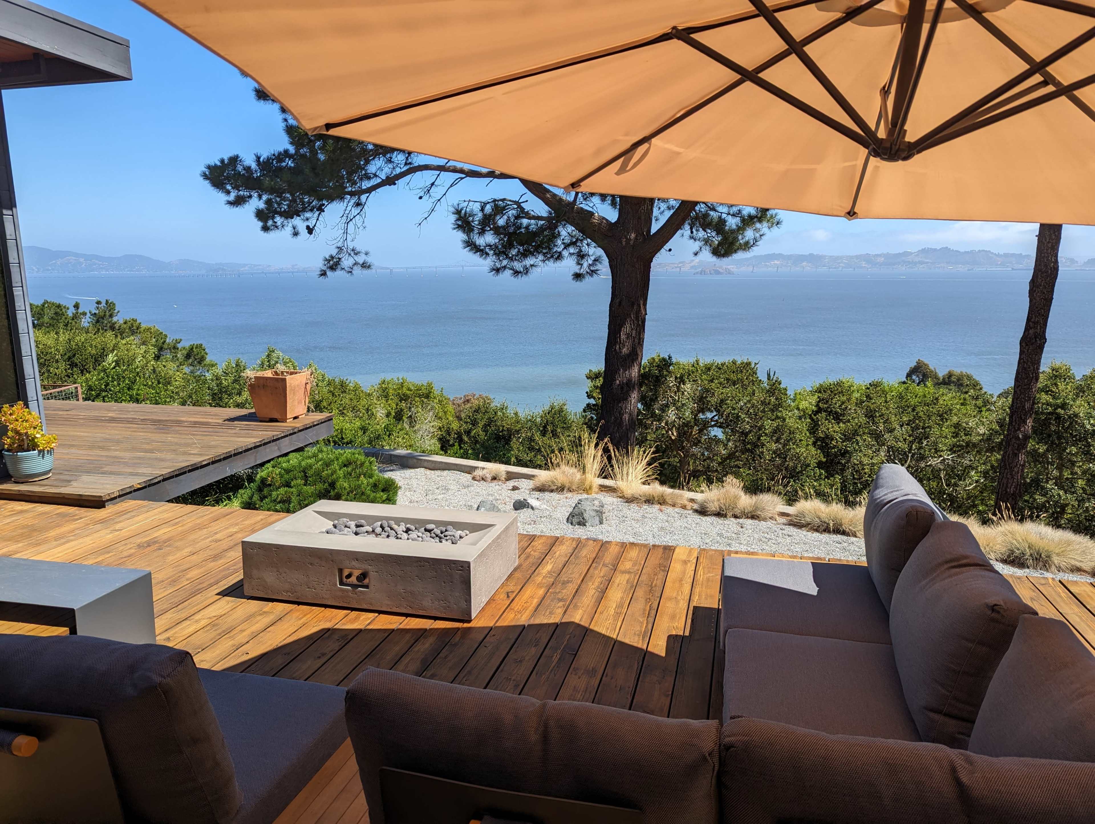 A shaded patio with a view of the water is set with a fire pit and comfortable seating.