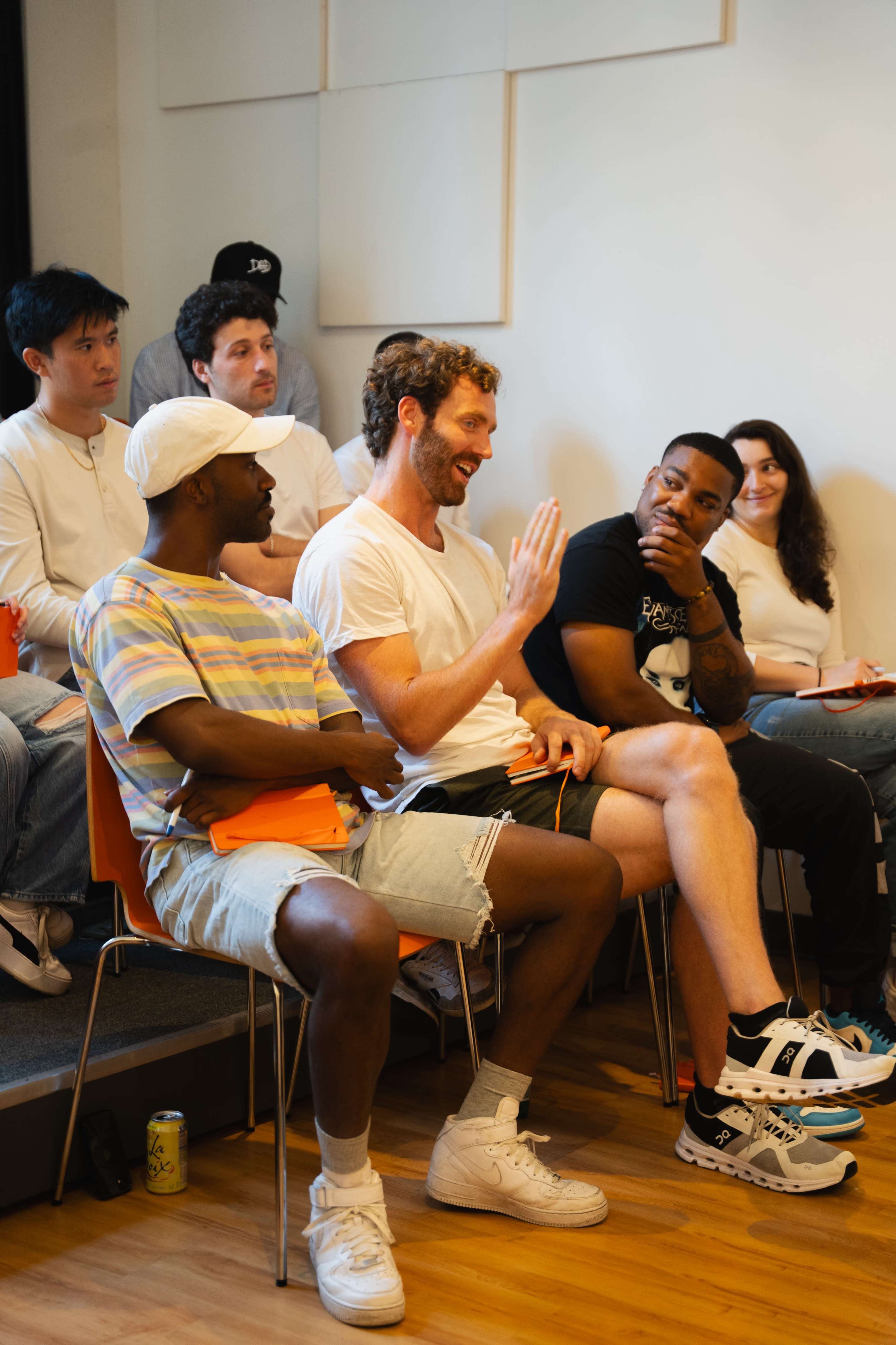A group of people are seated in a casual setting, with one man speaking while others listen attentively.