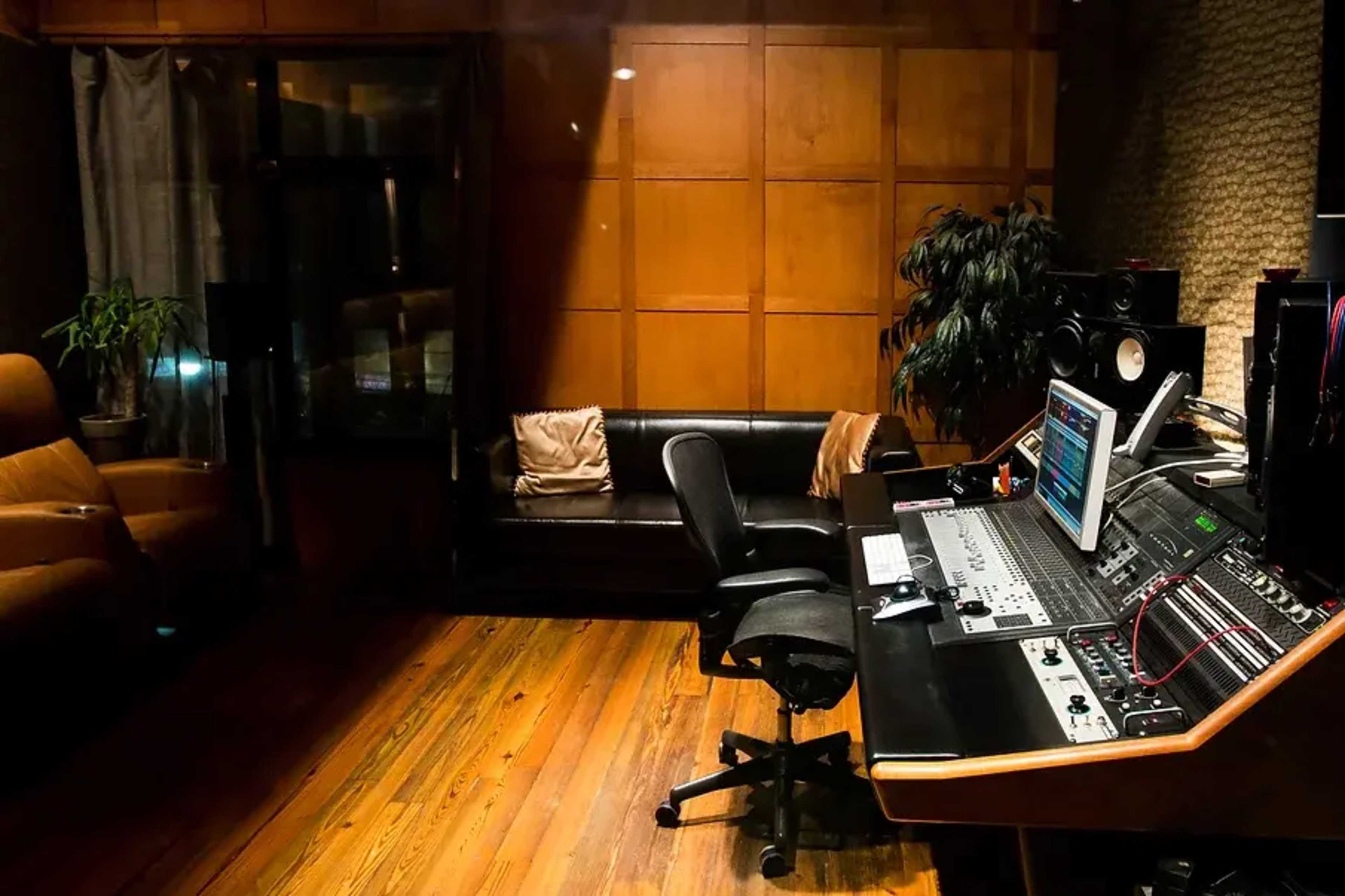 A music recording studio with a mixing console, an office chair, a couch, and wooden paneling on the walls.
