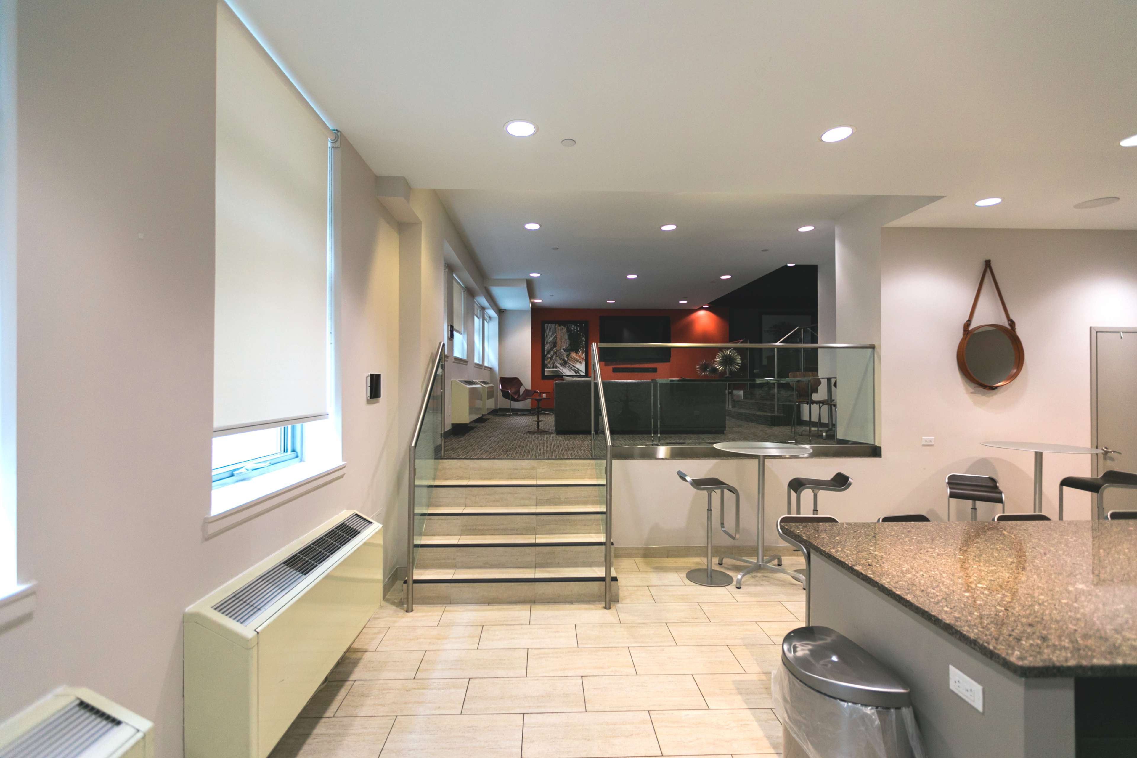 A modern, multi-level interior space with a staircase leading to a lower area, a kitchen counter, and a seating area.
