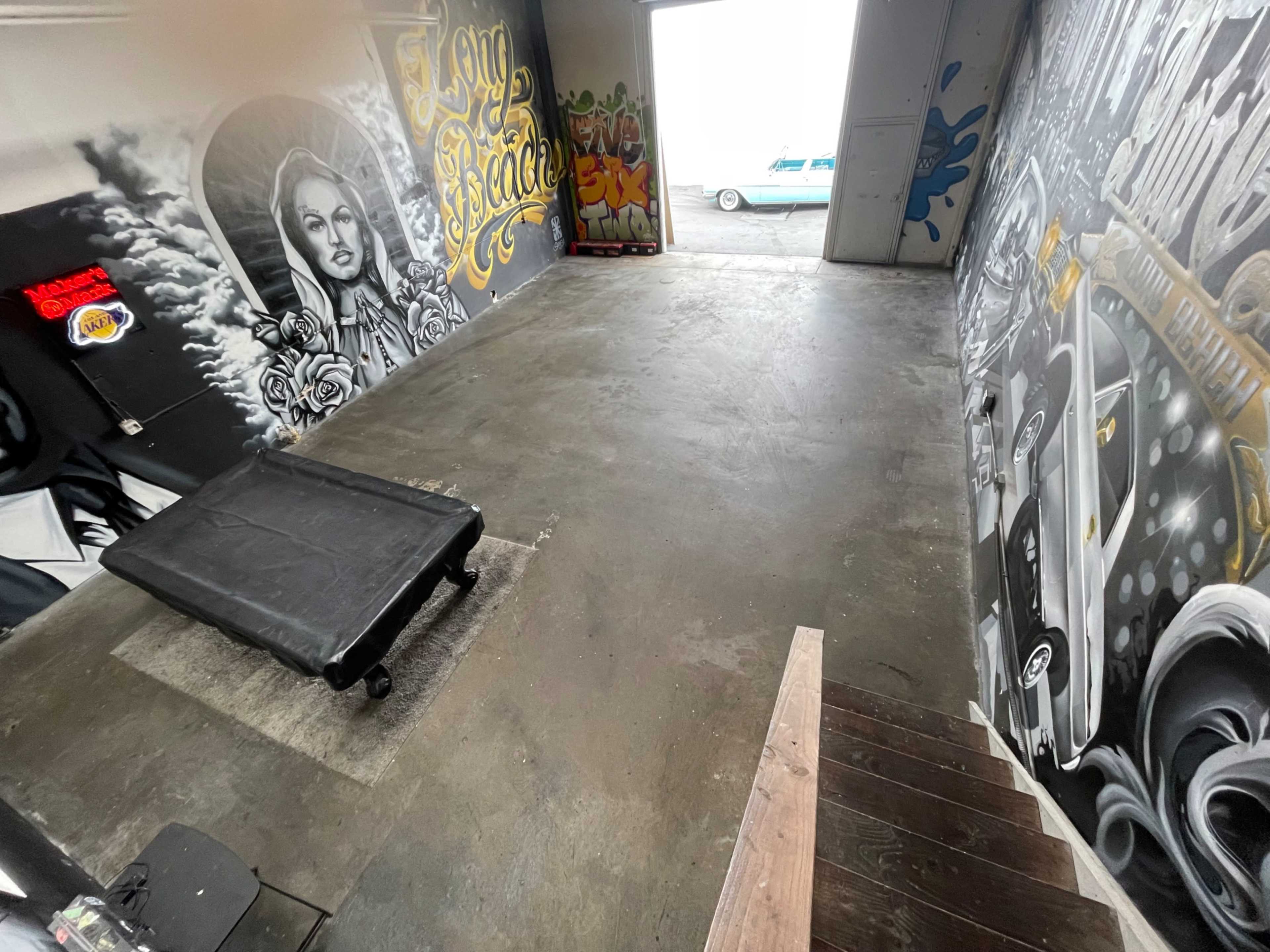 A spacious garage with graffiti-covered walls and a black cart on the floor, leading to an open exit.