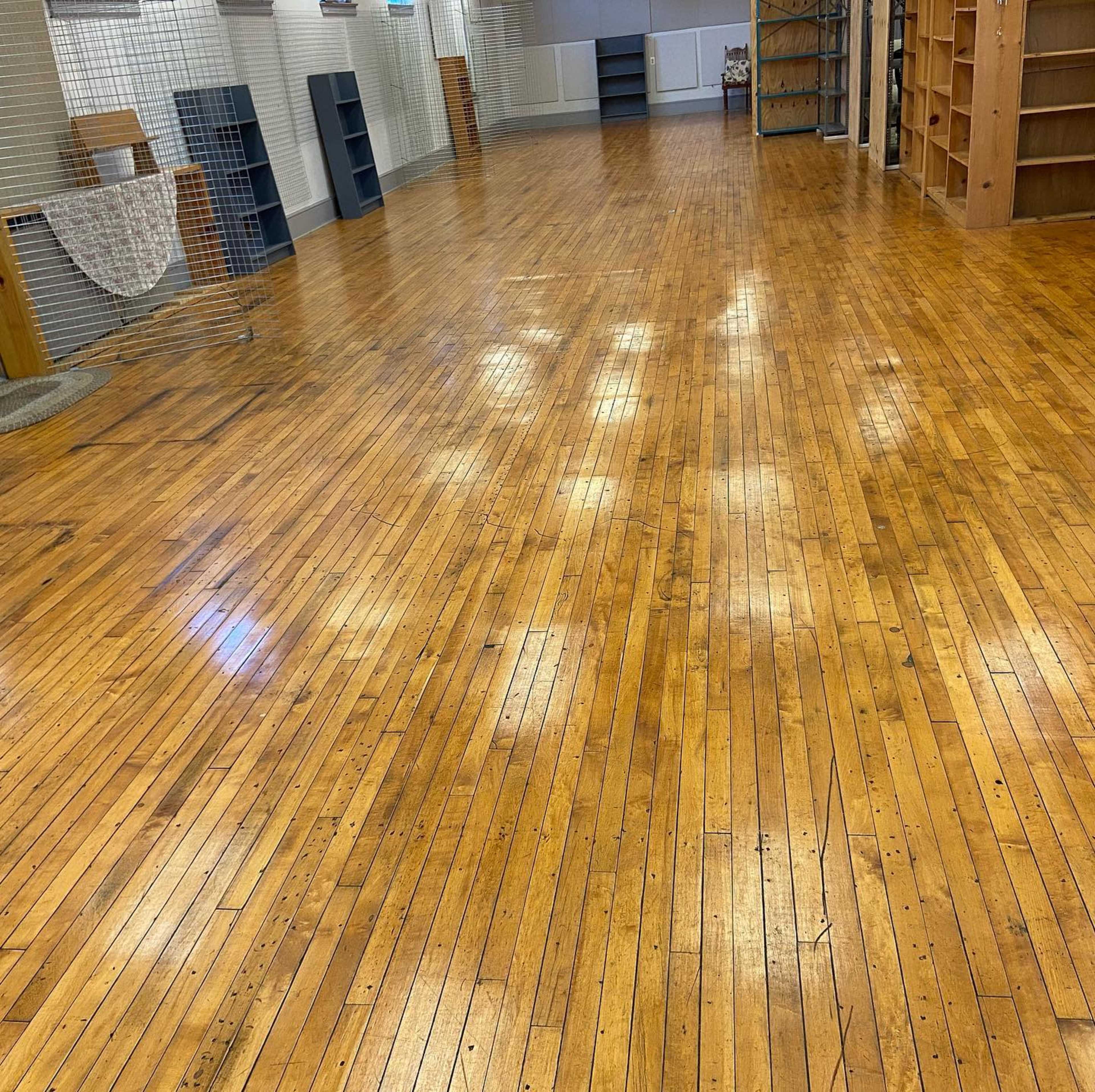 The image shows a spacious room with polished wooden floors and empty bookshelves along the walls.
