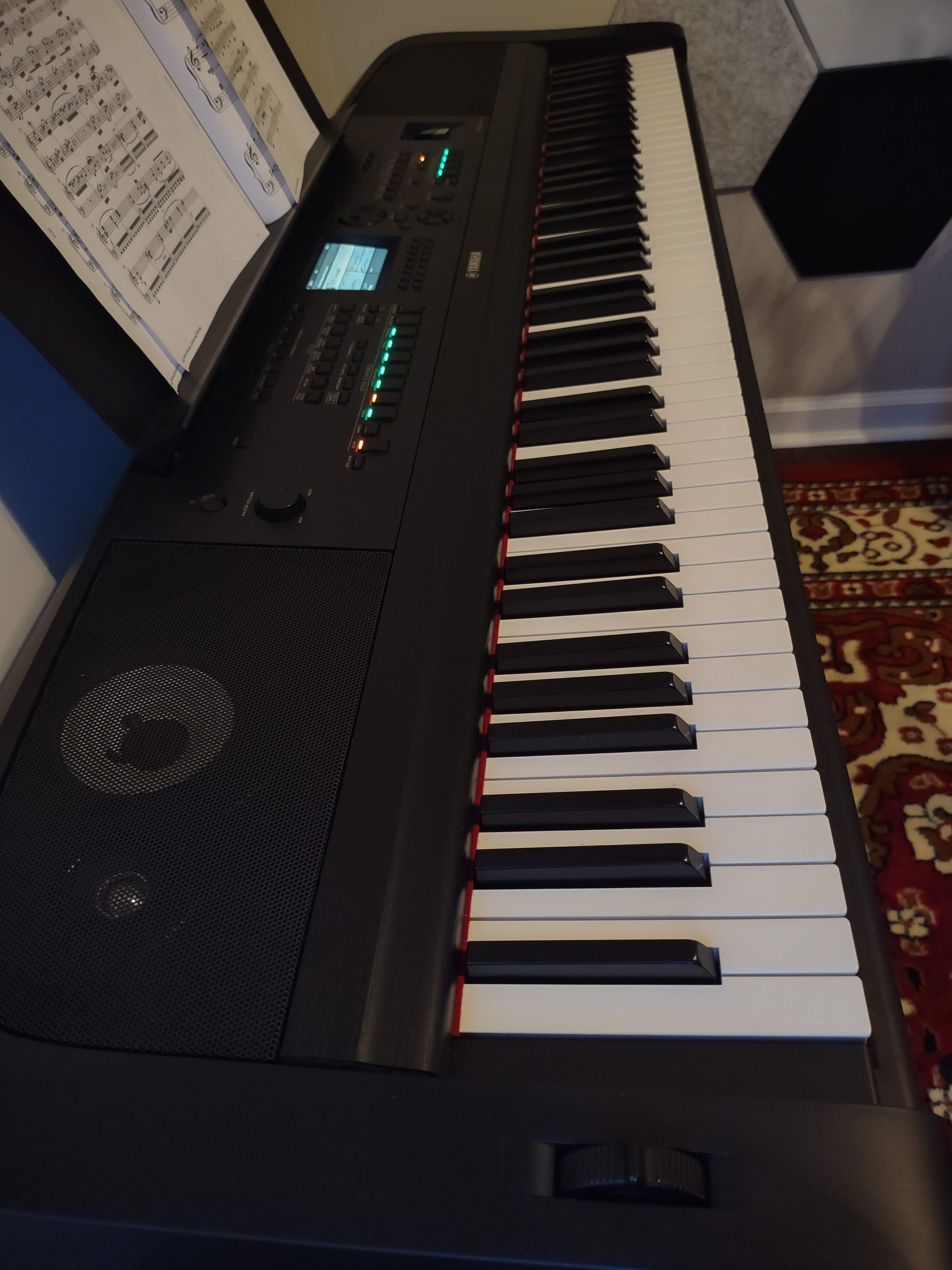 The image shows a black digital piano with visible keys, a control panel, and sheet music displayed above it.