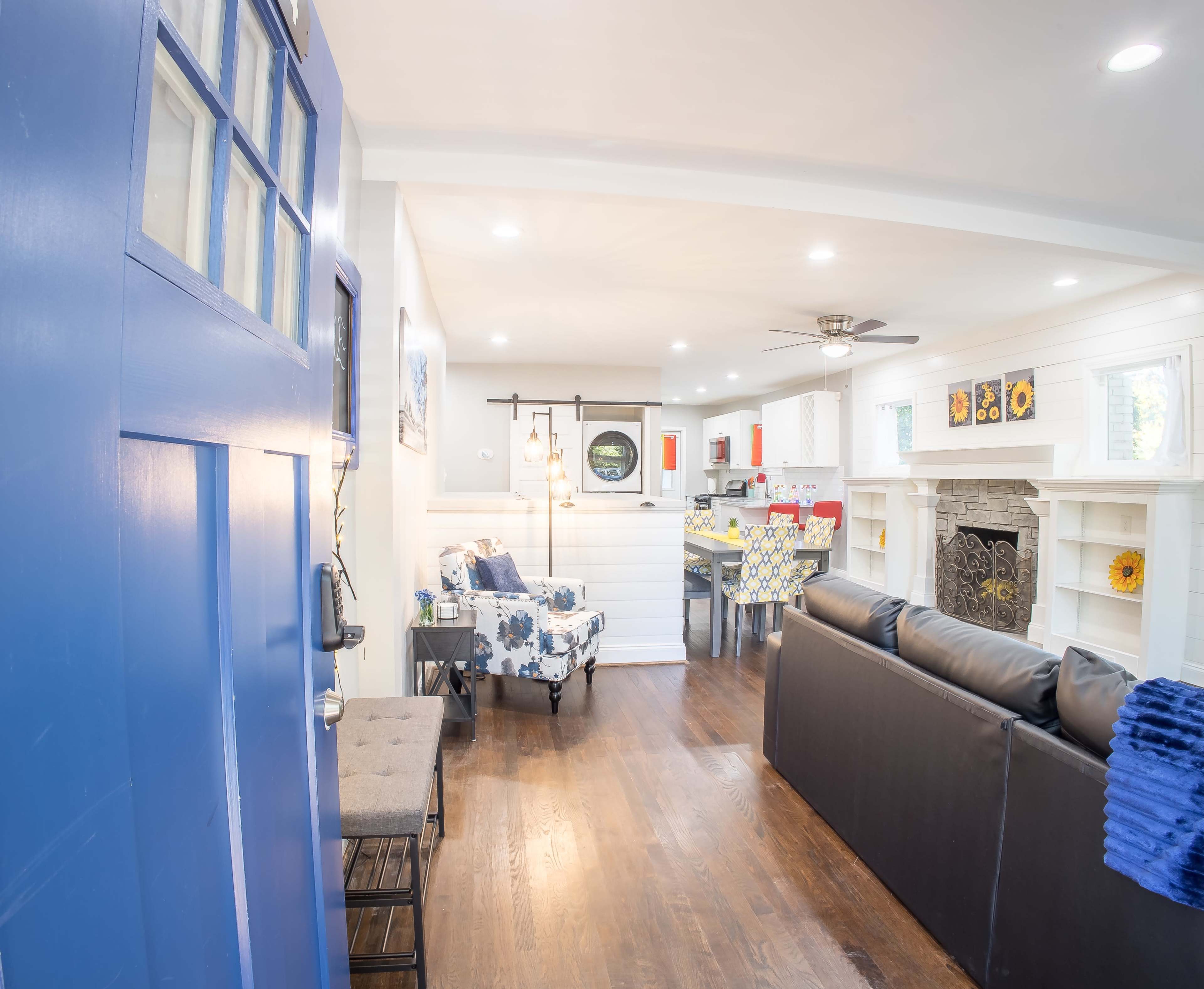A bright, open living space with a blue front door leading to a seating area and a visible kitchen in the background.
